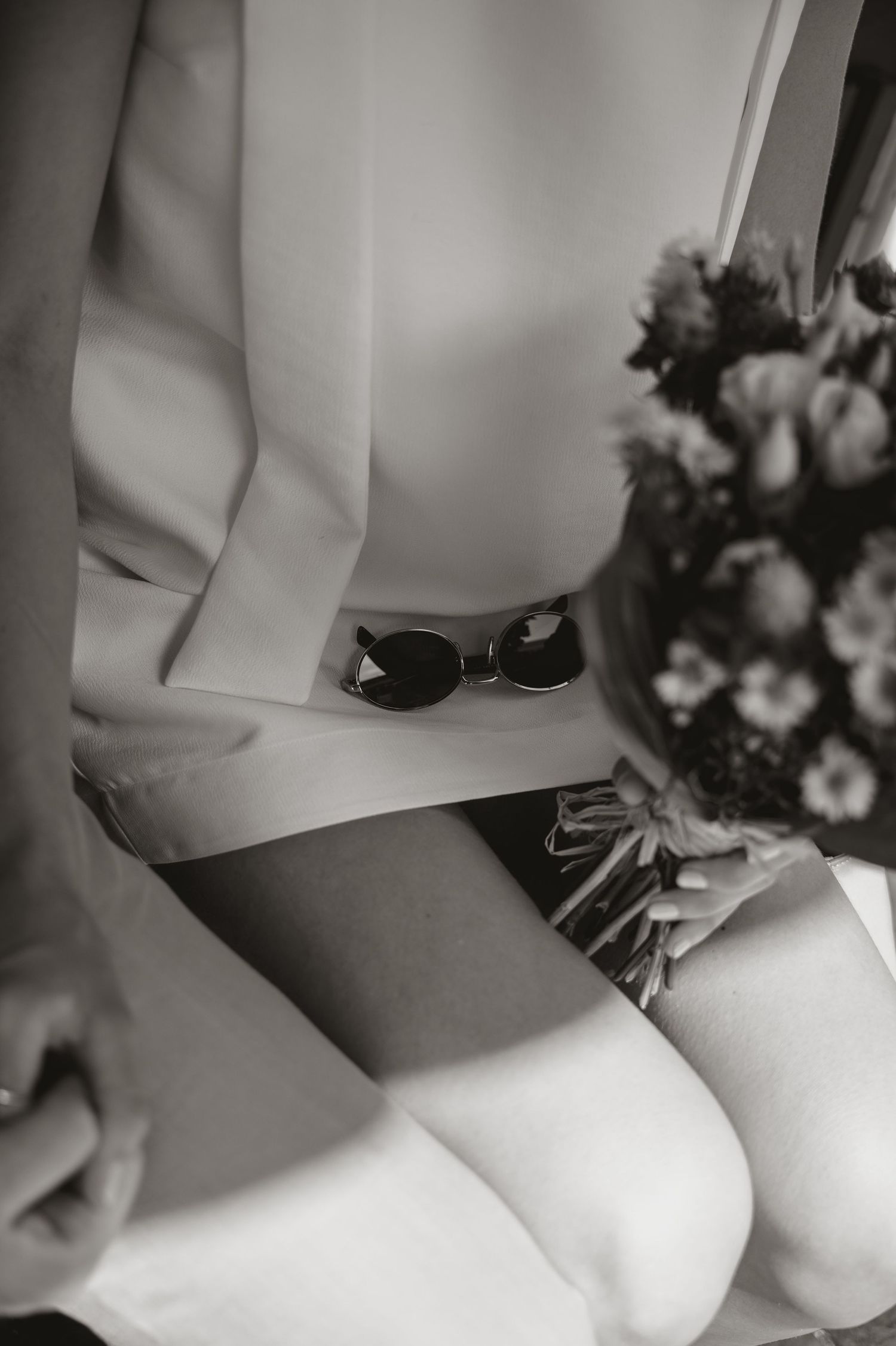 Black and white close-up photograph of a bride's hands holding a delicate bouquet of white flowers.
