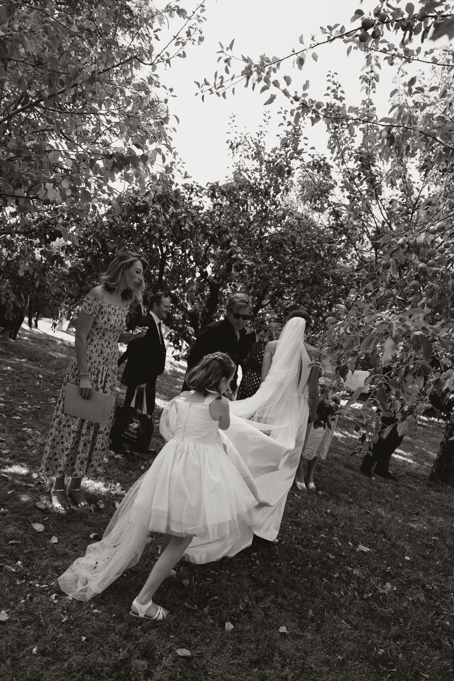 A couple in wedding attire sits together under blooming trees in a romantic outdoor setting.