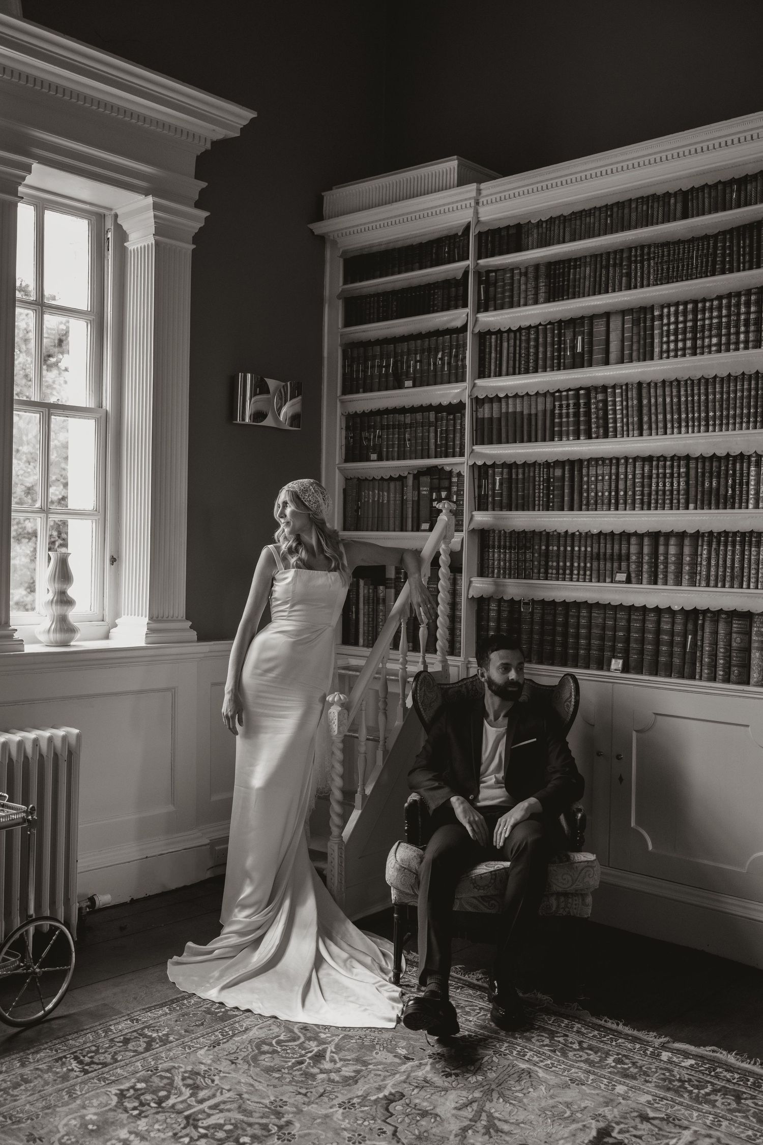 Vintage library interior with tall bookshelves, ornate molding, and figures arranging books in black and white photography.