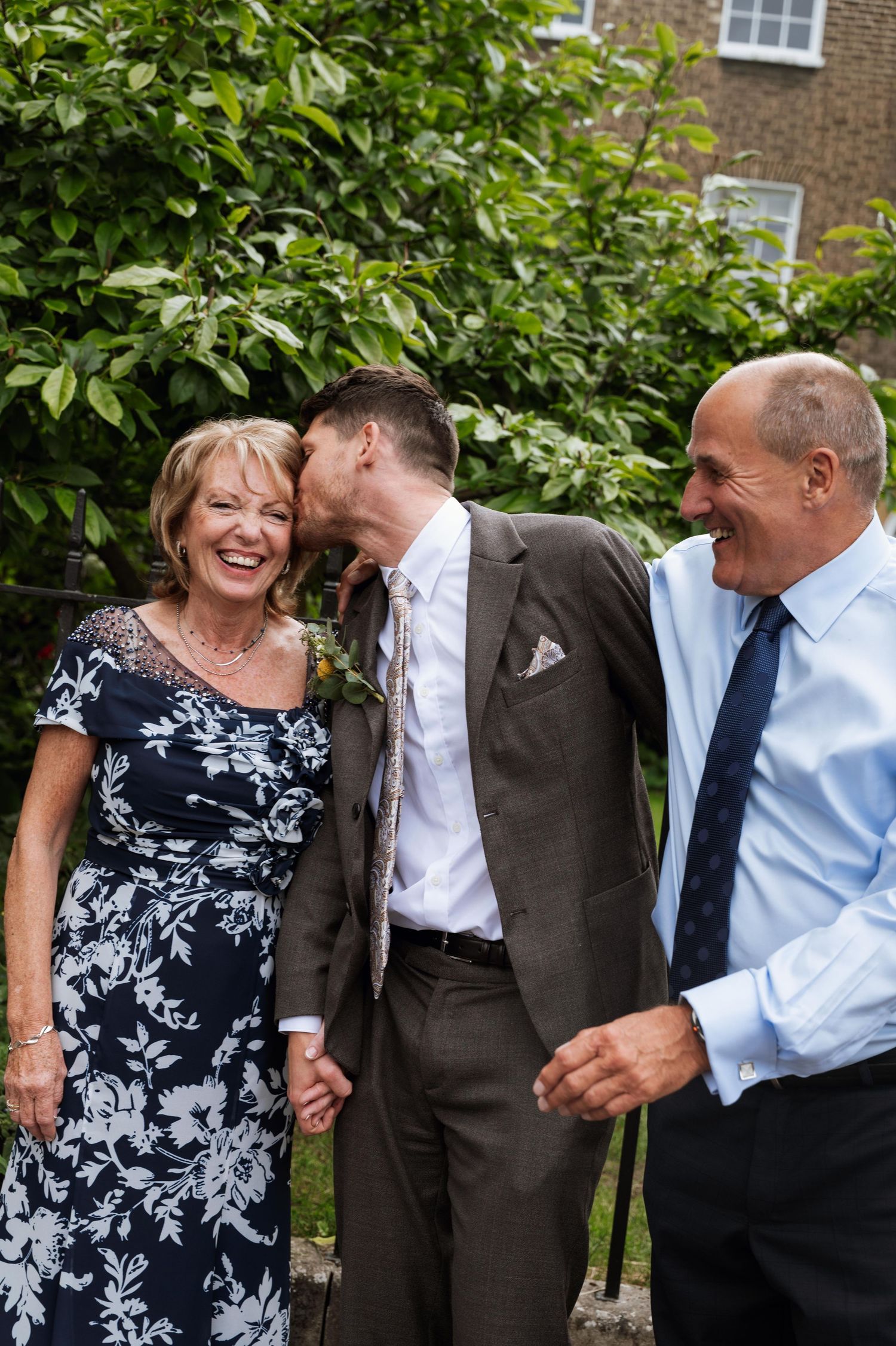 A joyful moment shared between wedding guests in a garden setting with brick building in background.