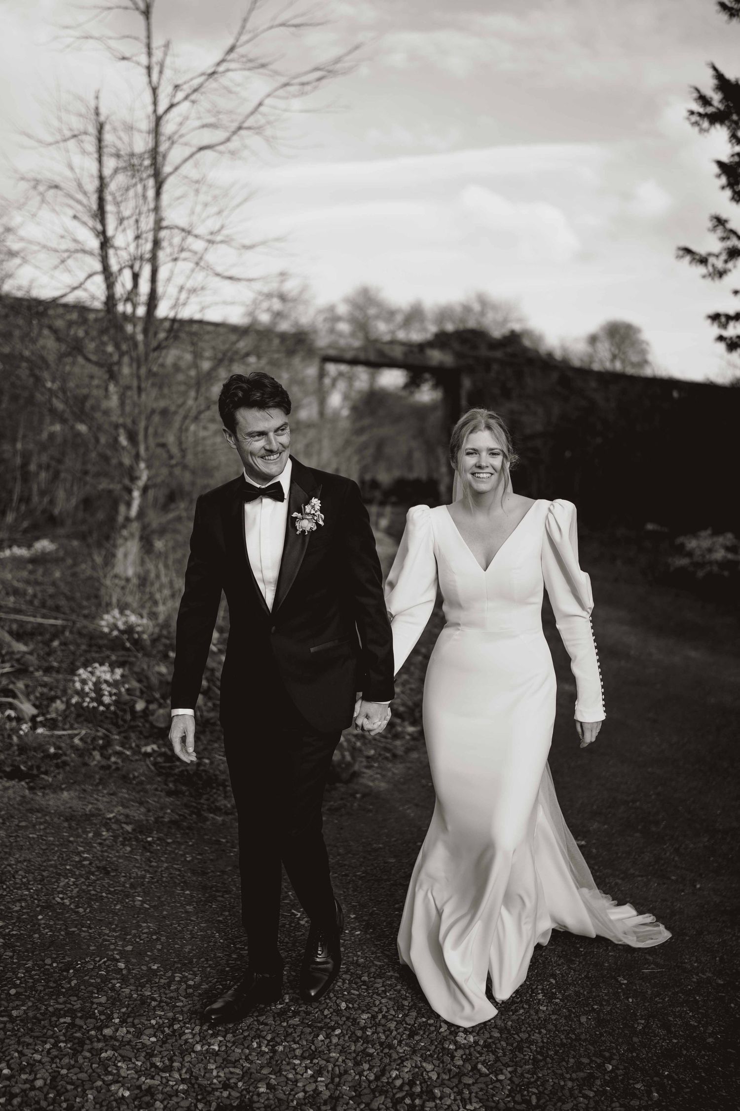A black and white wedding photo series showing a couple walking and laughing together in a natural outdoor setting.