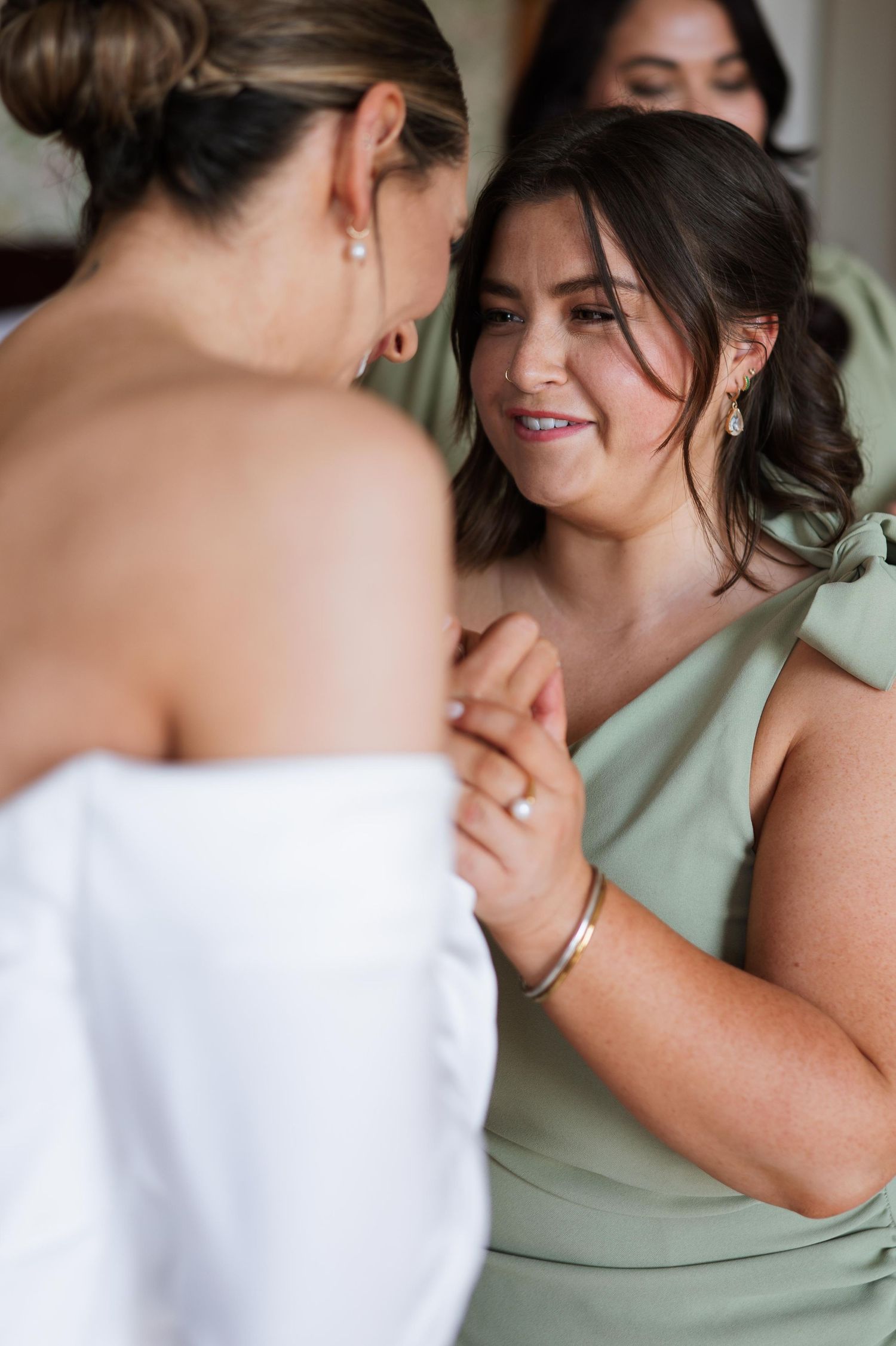 Two friends in an intimate moment share tender glances and smiles while wearing white and sage green attire.