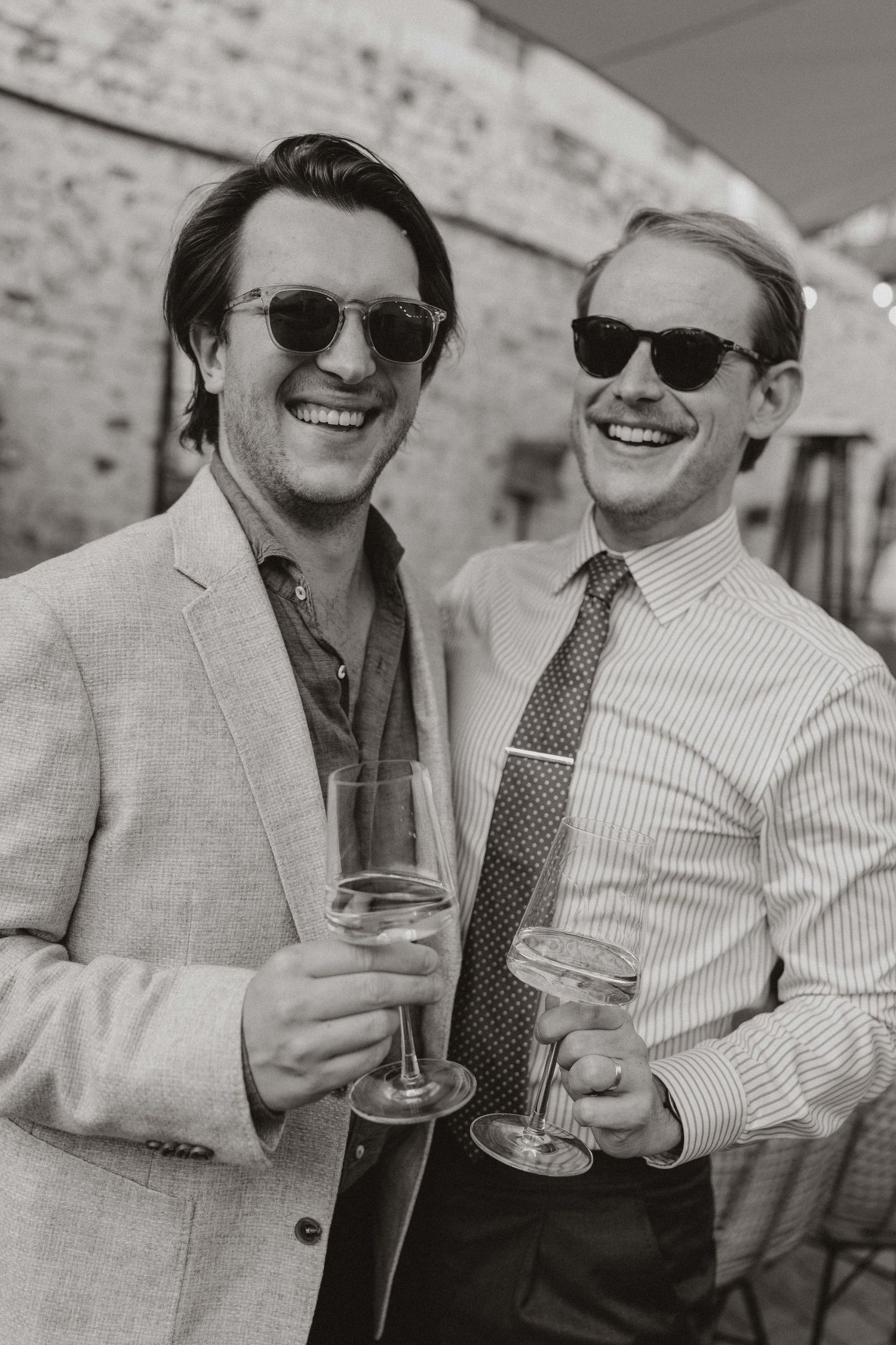 Two people wearing sunglasses share drinks and laughs in a series of black and white candid photos.