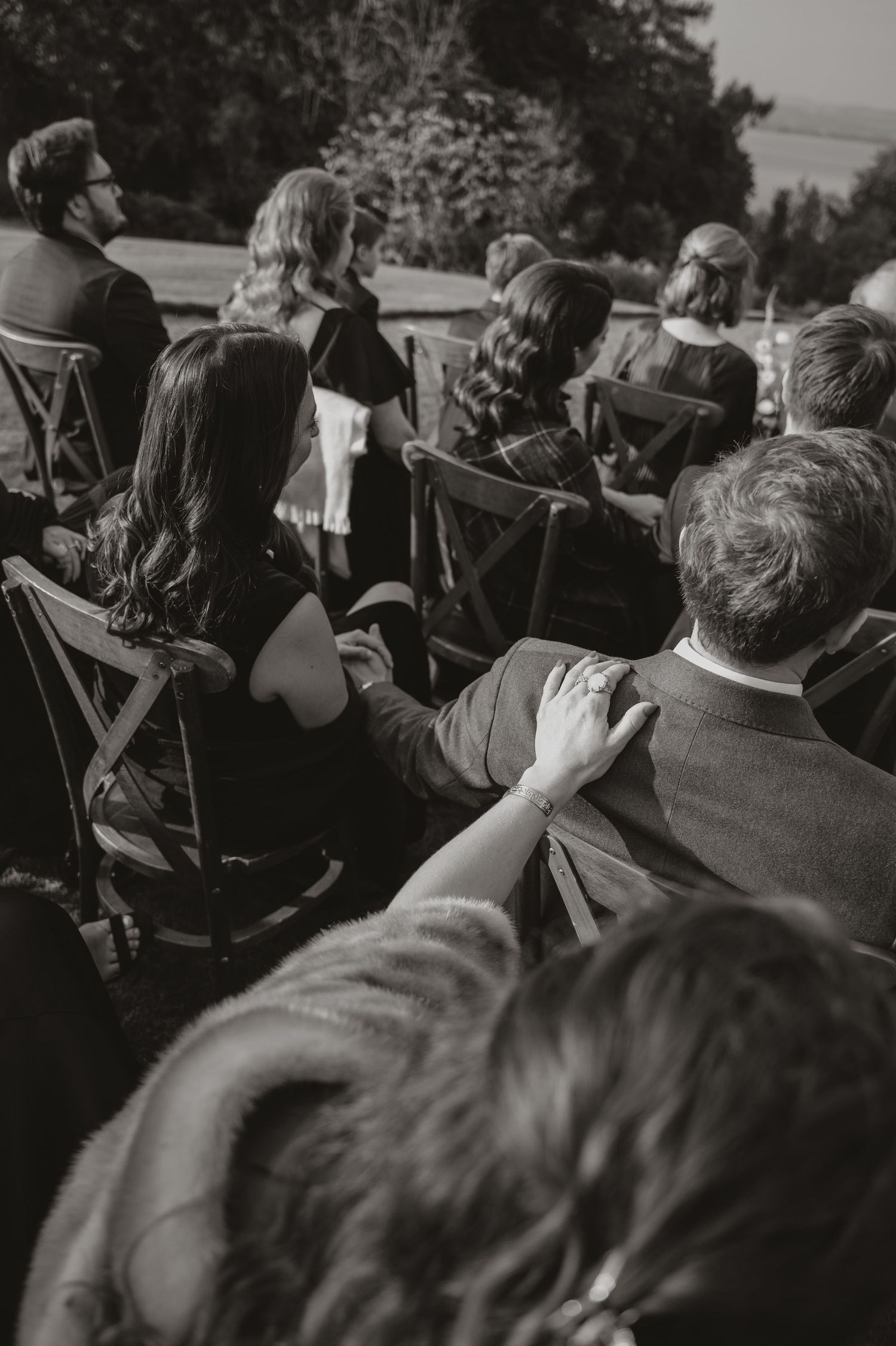 Black and white photo of a crowd sitting in chairs at an outdoor event, viewed from behind.