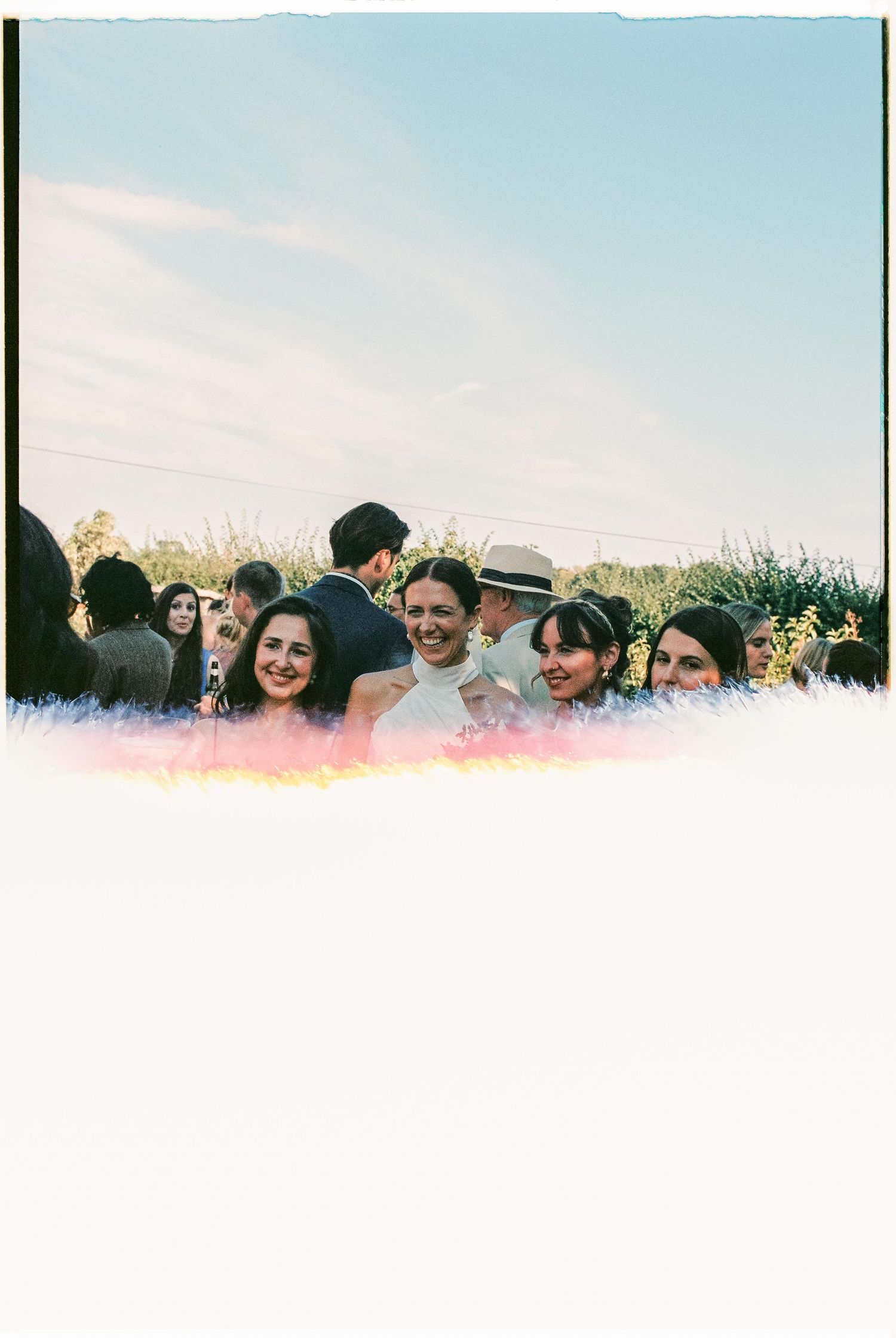 A group of people smiling together outdoors in a candid panoramic shot at sunset.