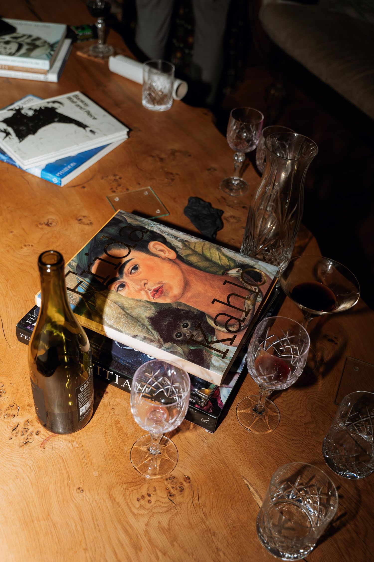 Empty wine glasses and bottles scattered on a wooden table surface in dim lighting.