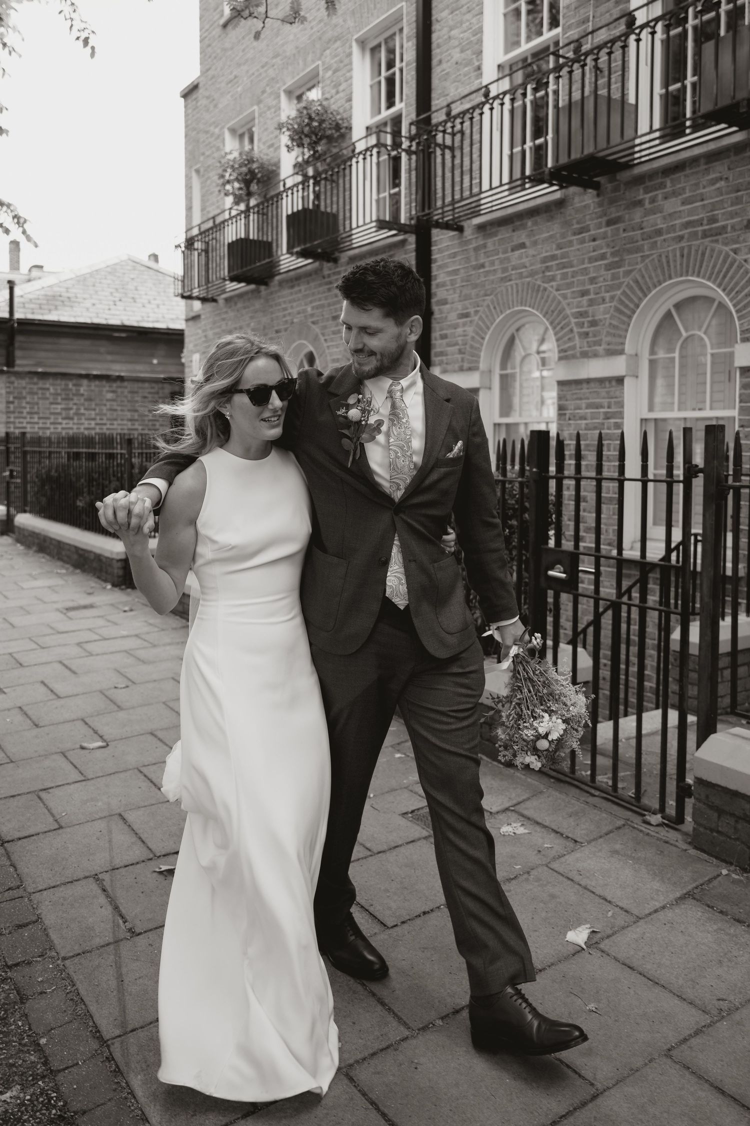 A series of four black and white wedding photos showing a couple dancing playfully on a city sidewalk.