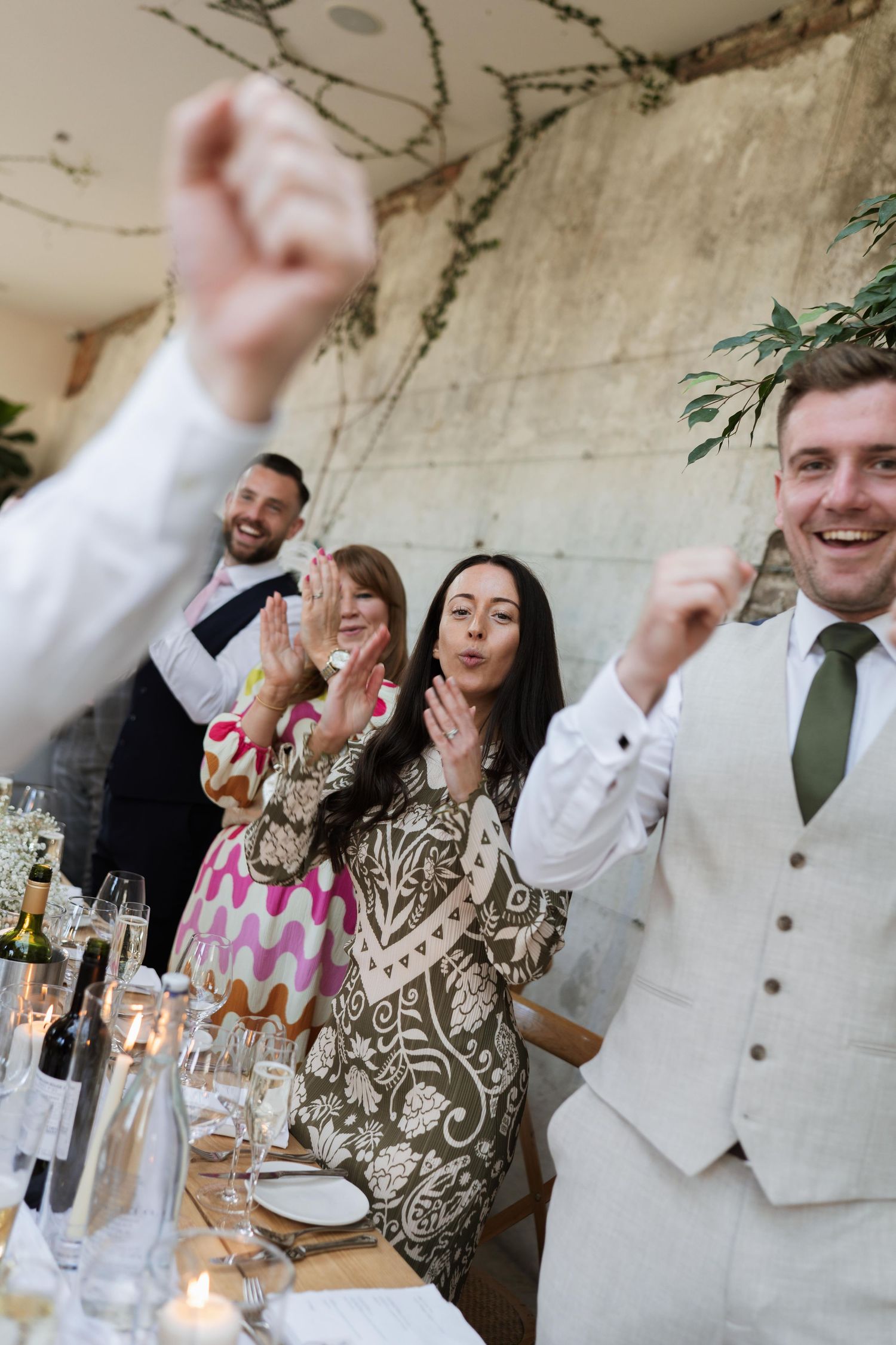Guests clapping and celebrating at a wedding reception dinner table with candles and wine glasses.