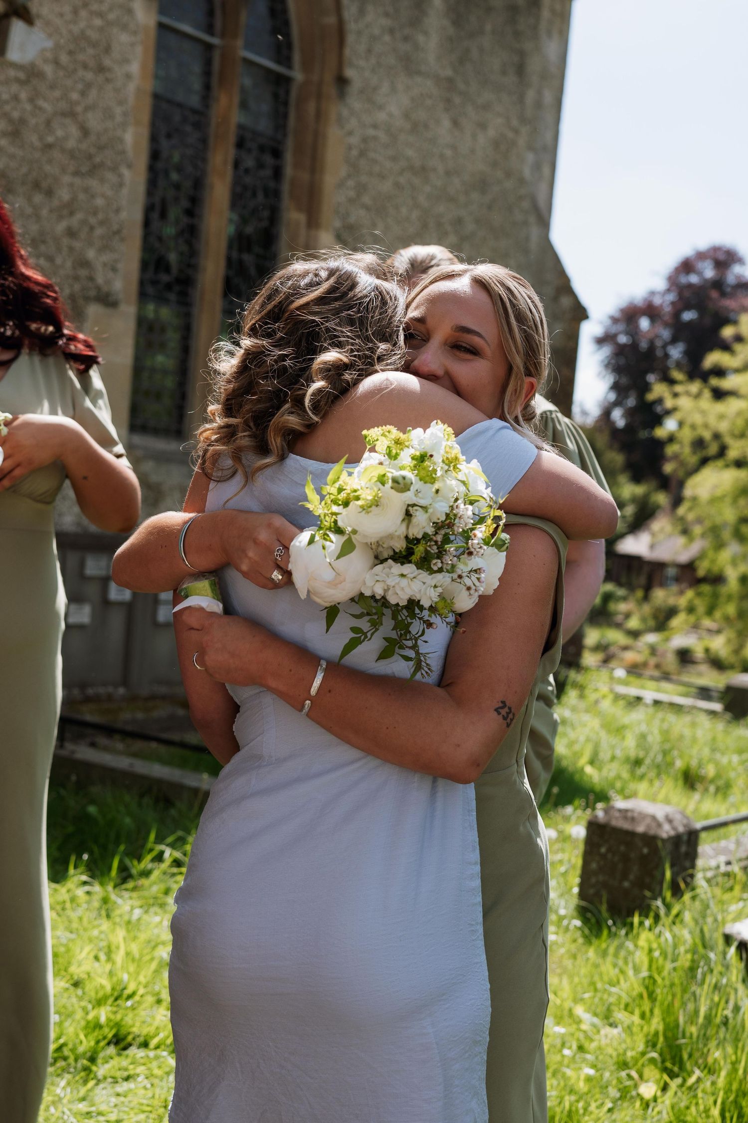 Three connected images show a tender embrace between two people in white dresses with flowers outdoors.