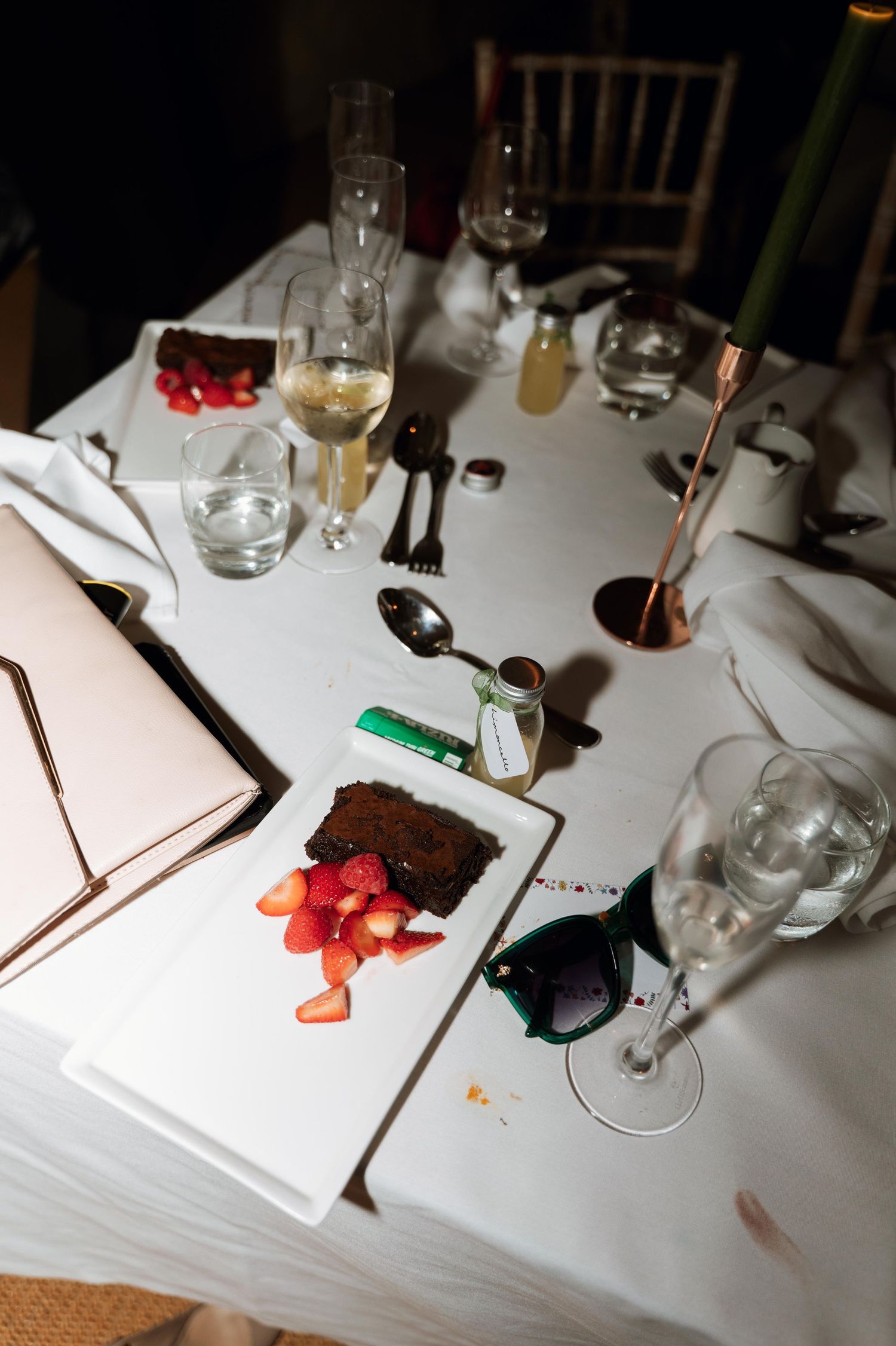 A table setting at a formal dinner with wine glasses, dessert plate with chocolate cake and strawberries.