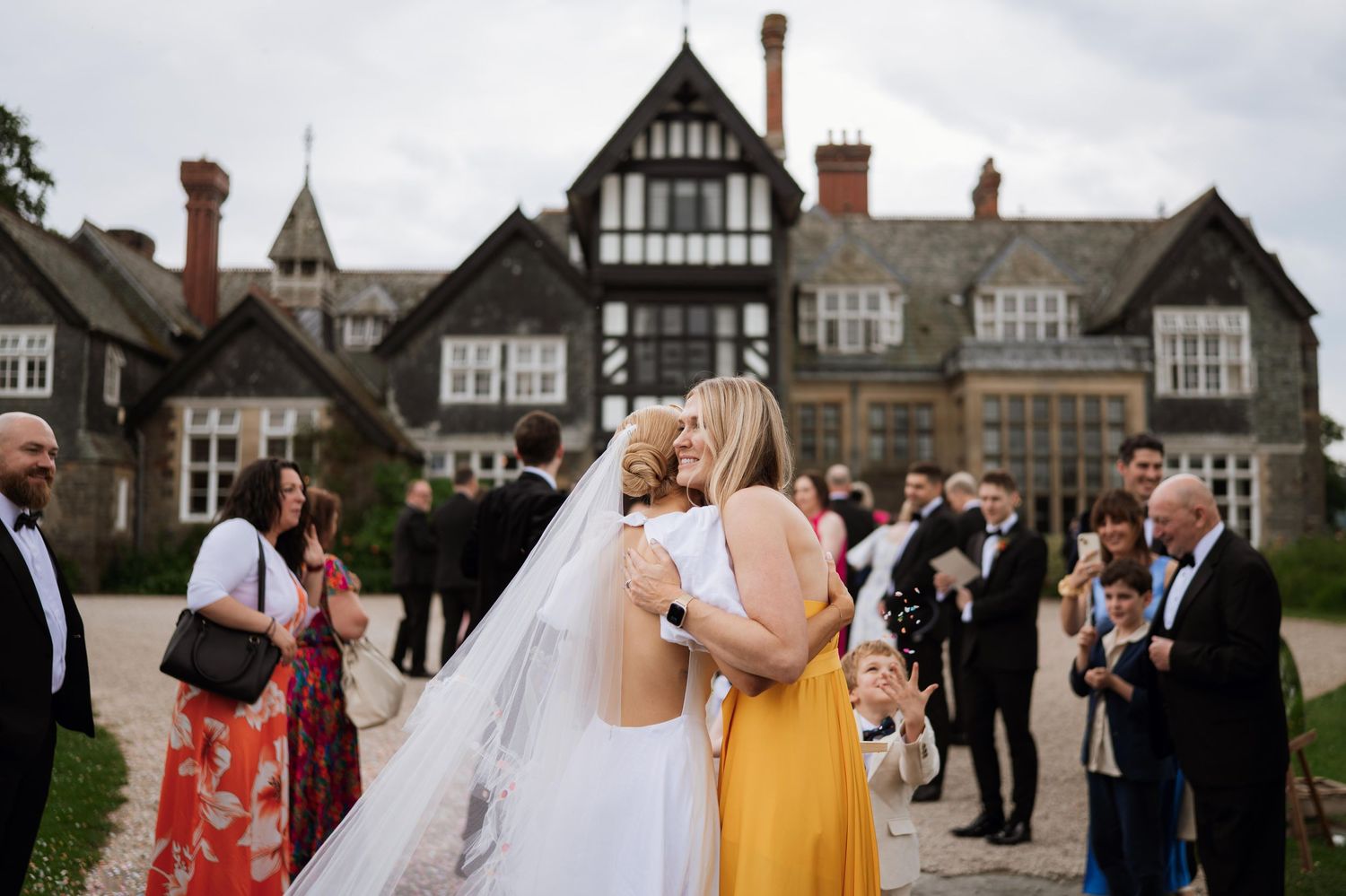 Wedding guests mingle and socialize on a patio outside a Tudor-style building during an elegant outdoor reception.