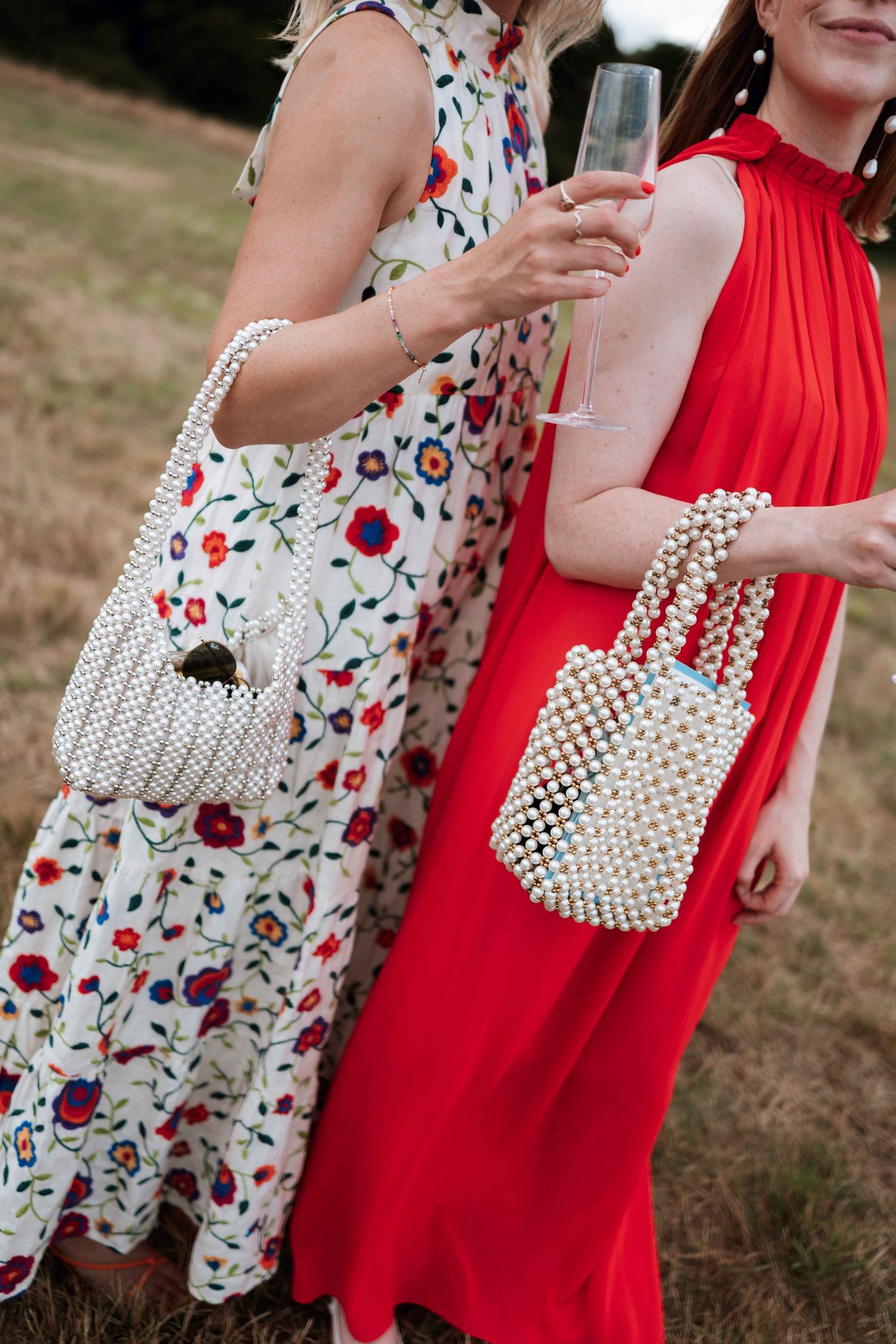People wearing floral print and red dresses carry beaded pearl handbags at an outdoor event.