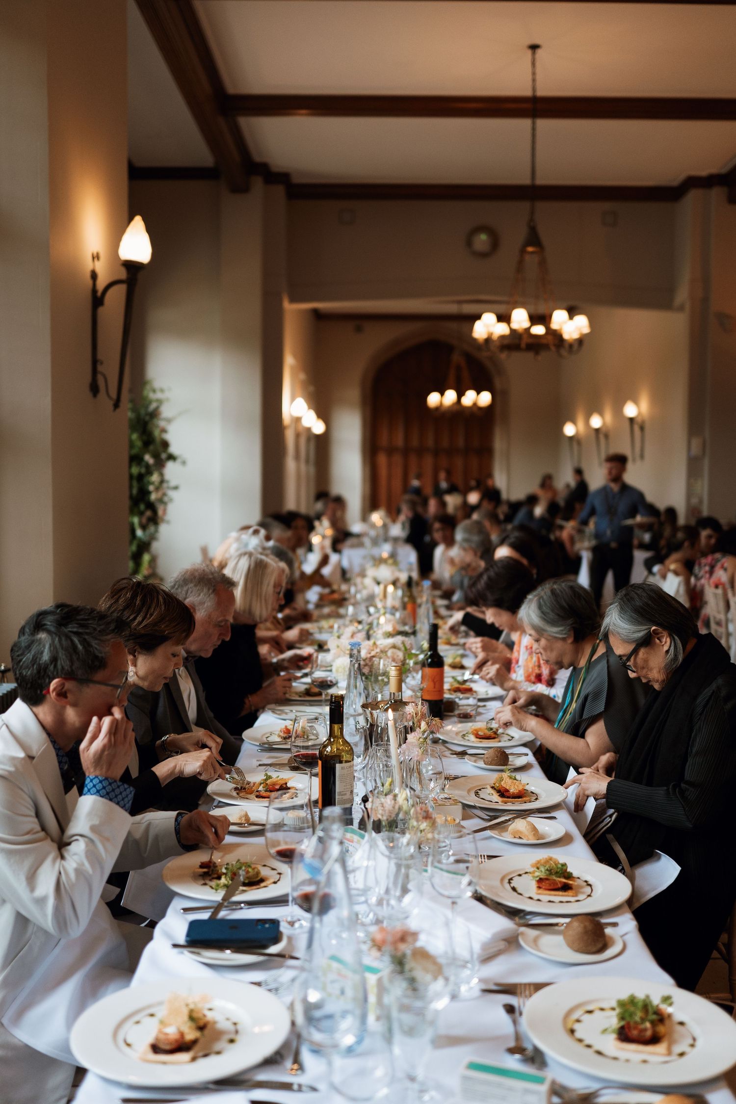 Diners seated at long tables at the elegant Ashridge House with chandeliers enjoying a formal meal service.