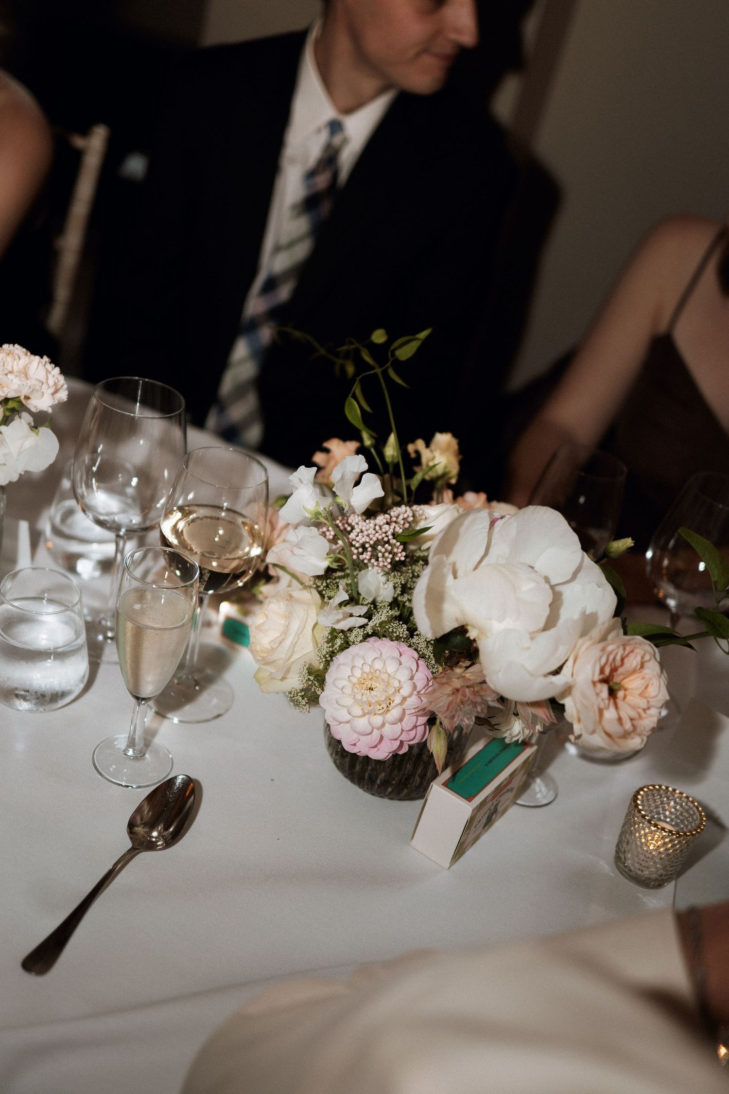 Elegant wedding table setting with blush roses, white hydrangeas, wine glasses and tealight candles on crisp white linens.
