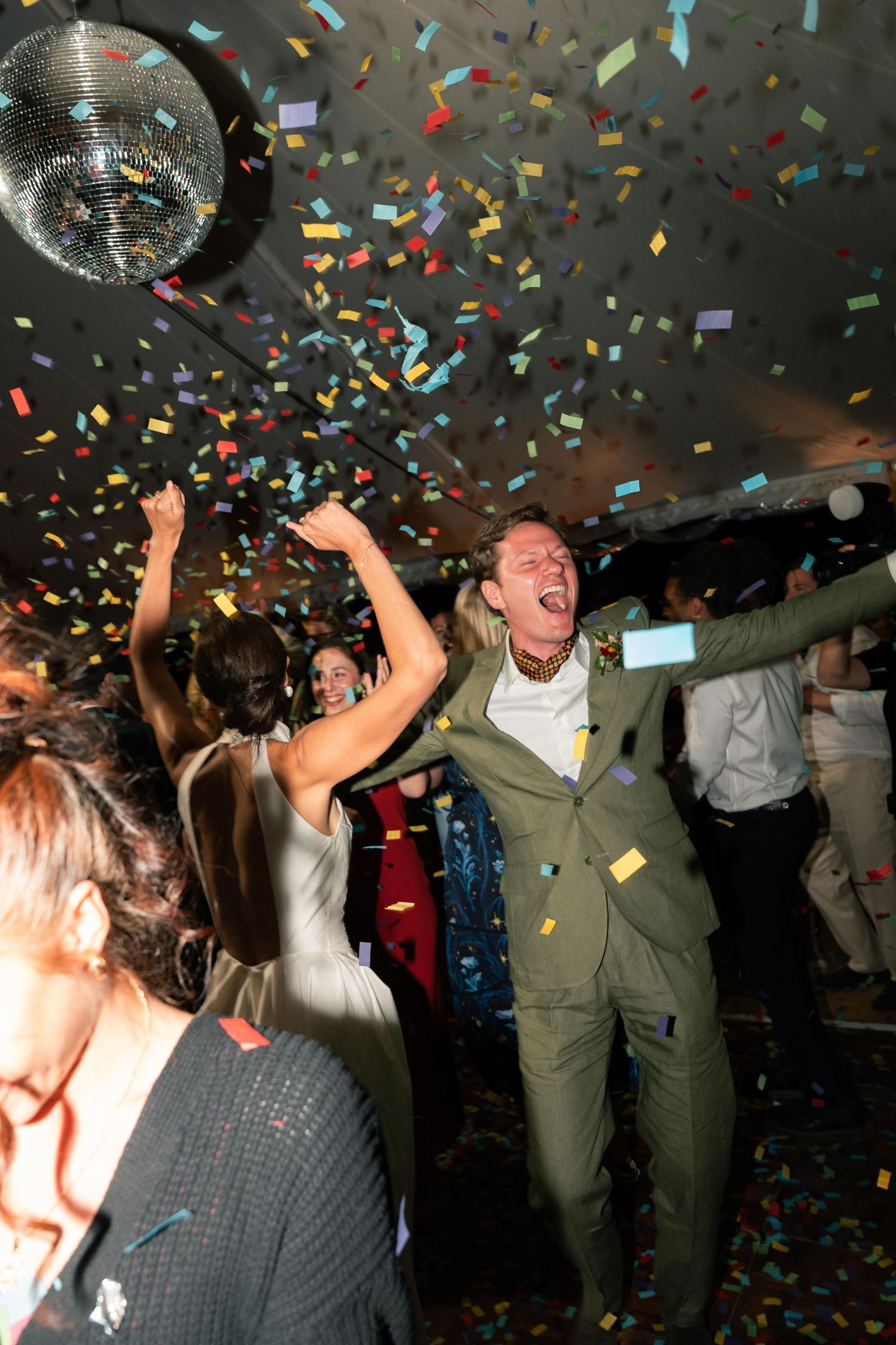 Colorful confetti rains down on a lively crowd dancing and celebrating at a party in a dark venue.