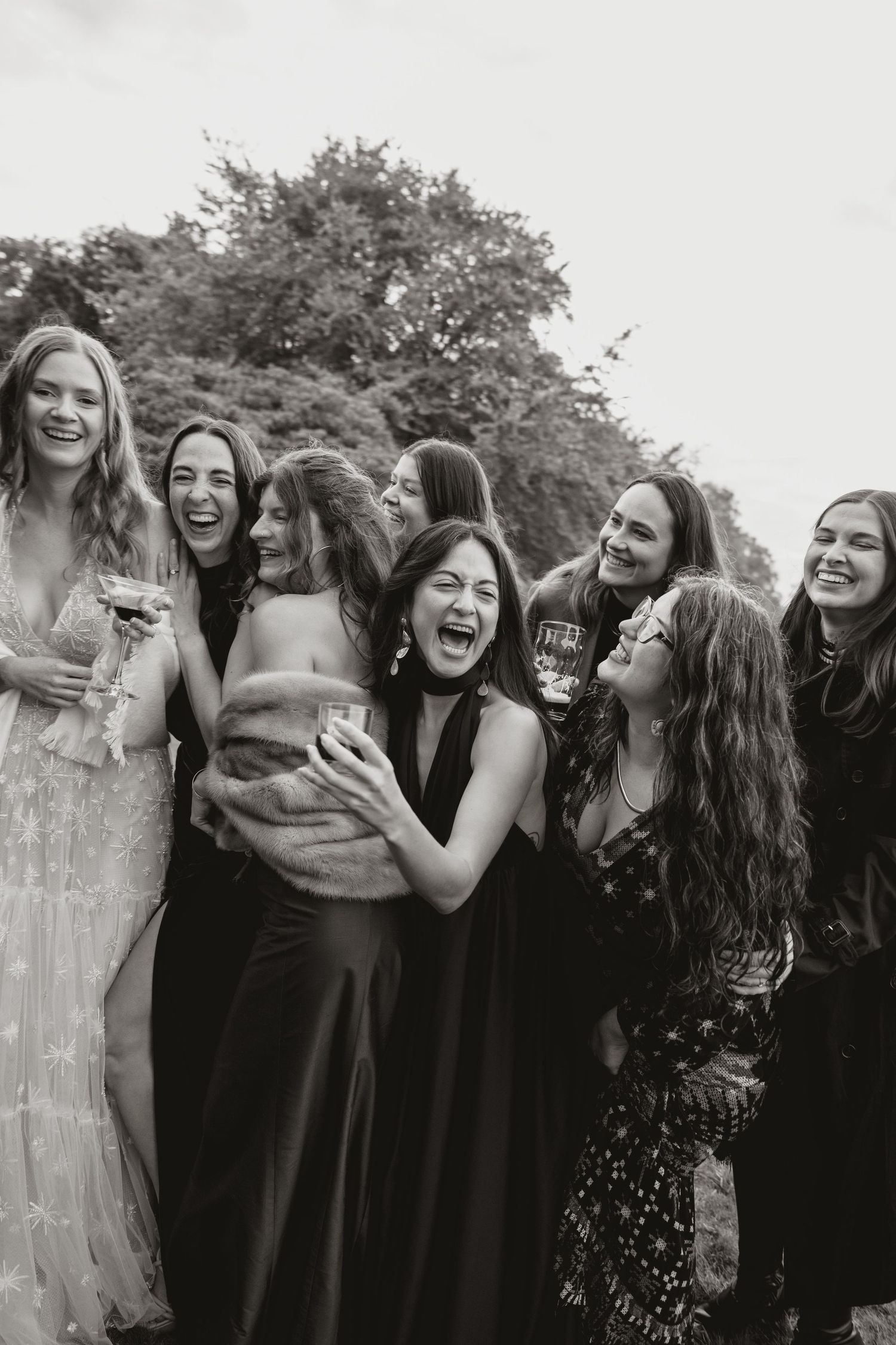 A group wearing black attire laughs together in a candid black and white photograph.