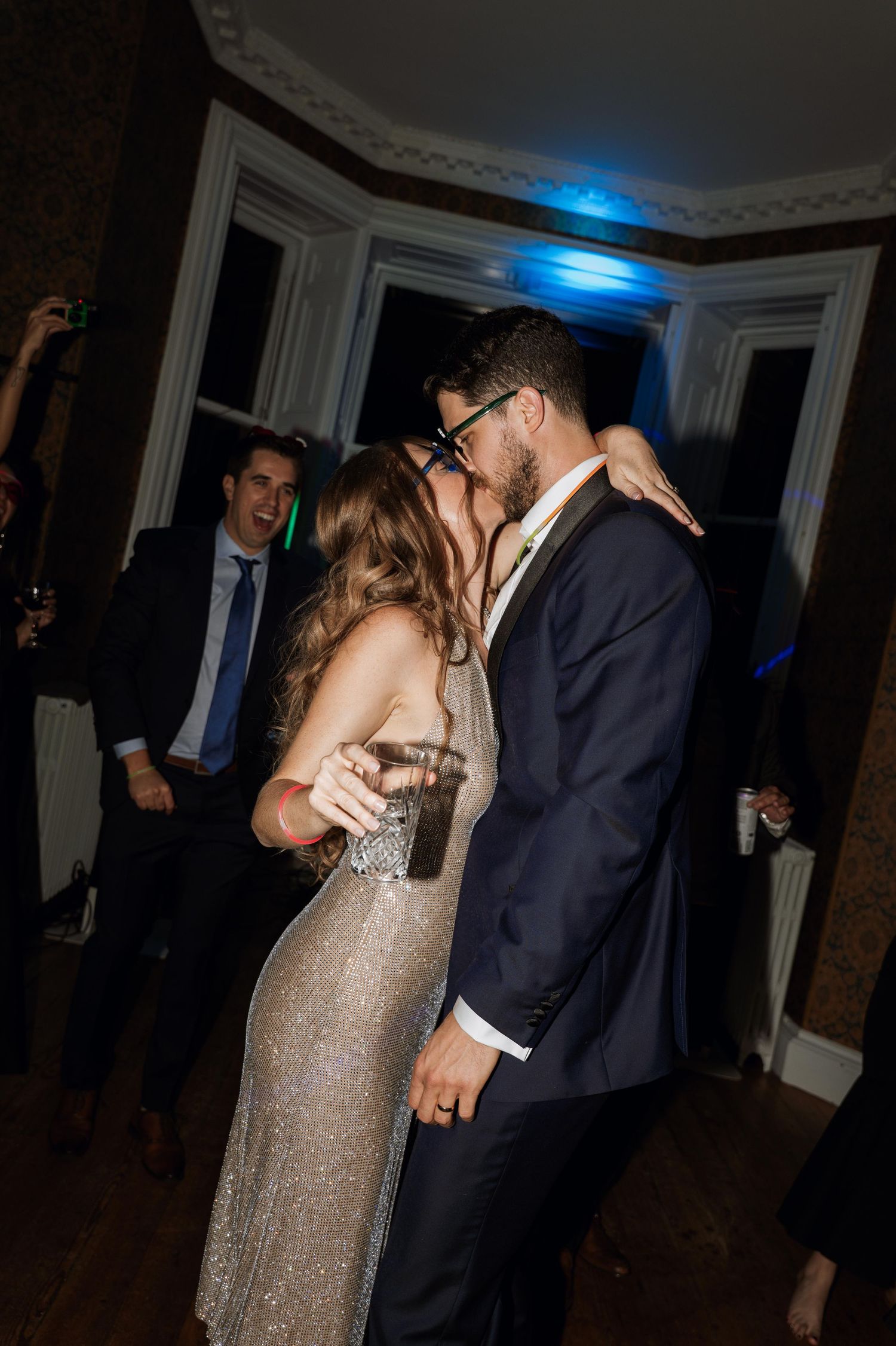 A couple shares a romantic dance moment in a dimly lit room with elegant crown molding and blue accent lighting.