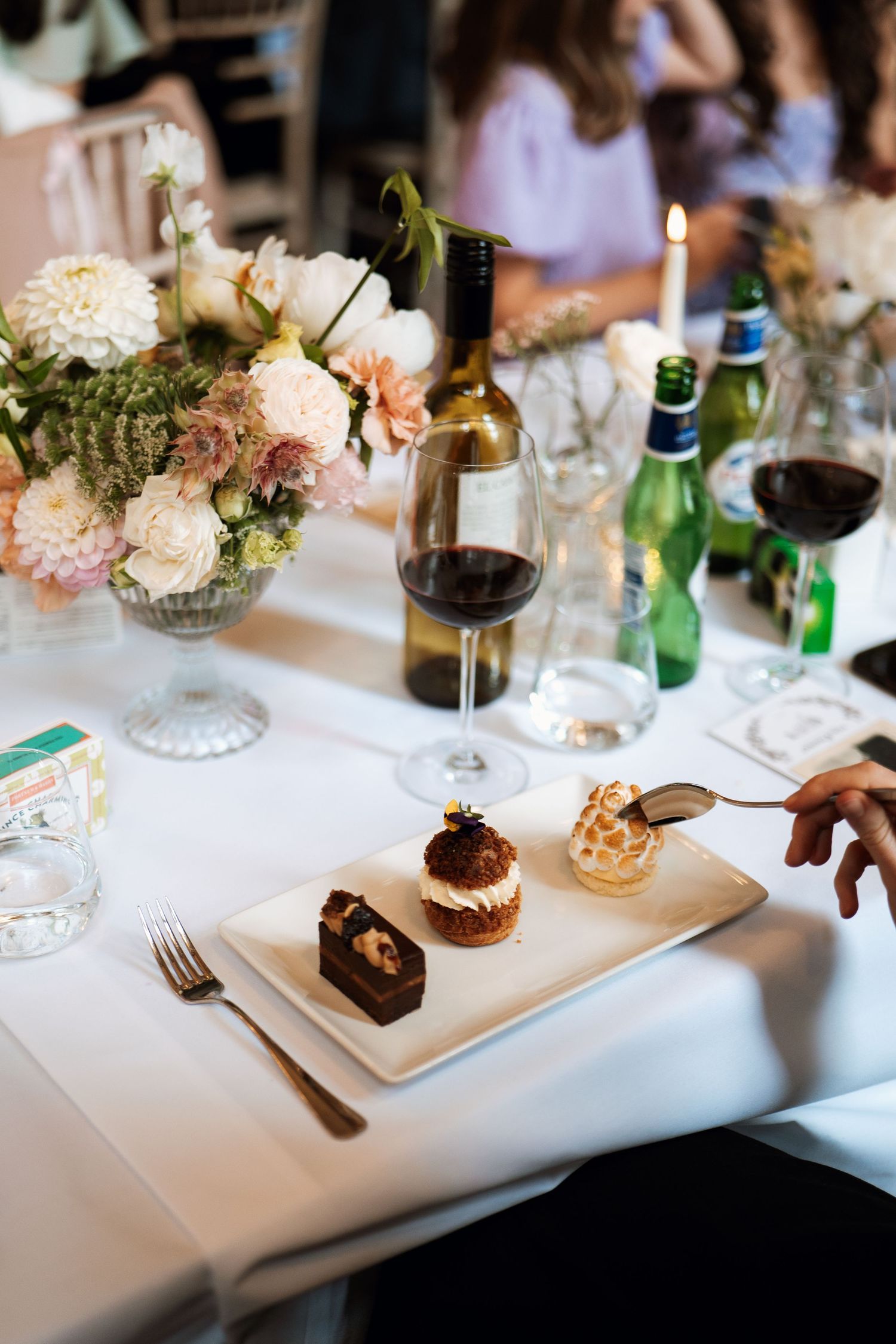 Chocolate dessert being served on white plates at an elegant dining table with wine glasses and floral centerpieces.