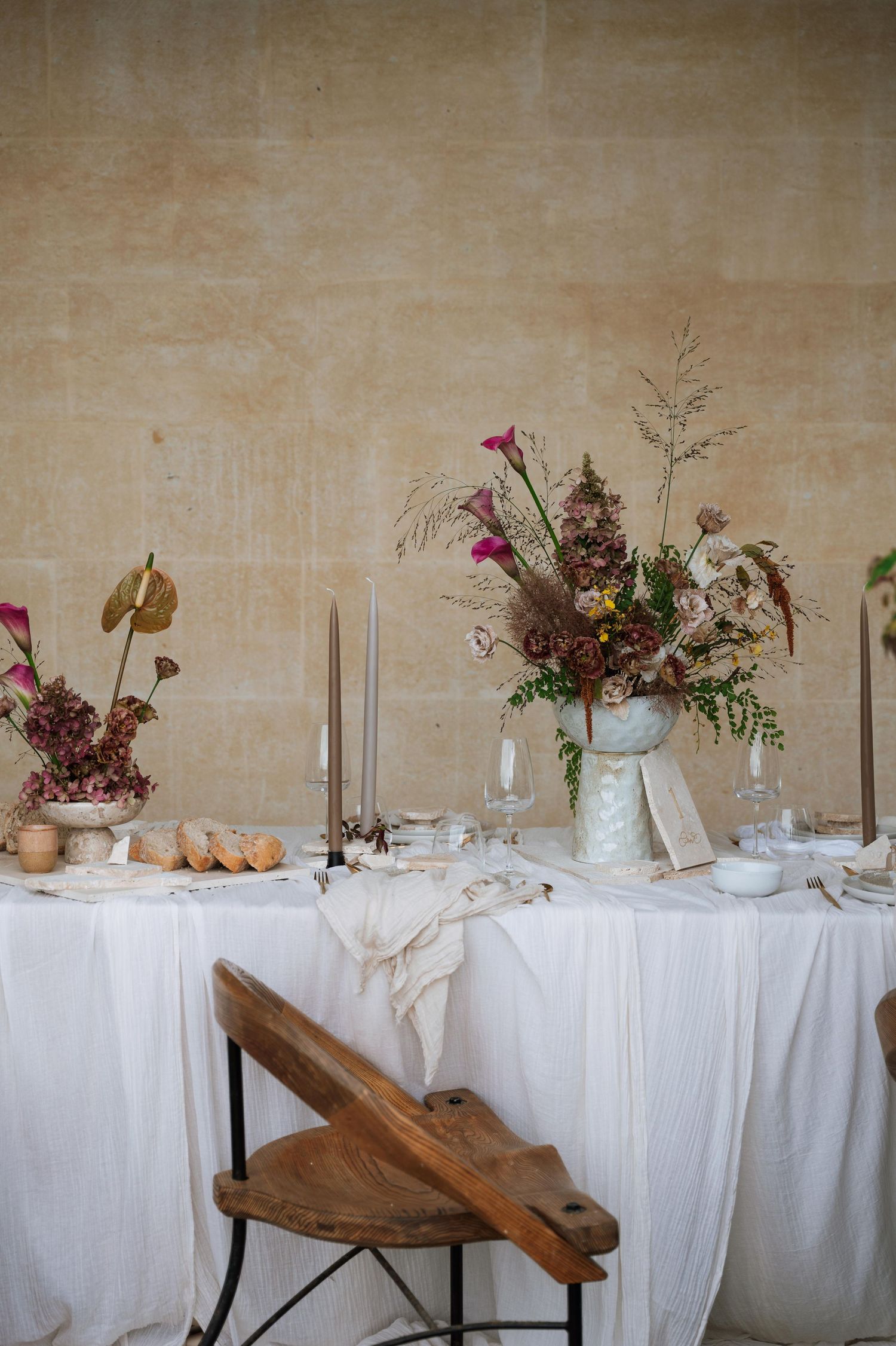 Long dining table with white tablecloth decorated with floral arrangements, candles, and rustic wooden elements.