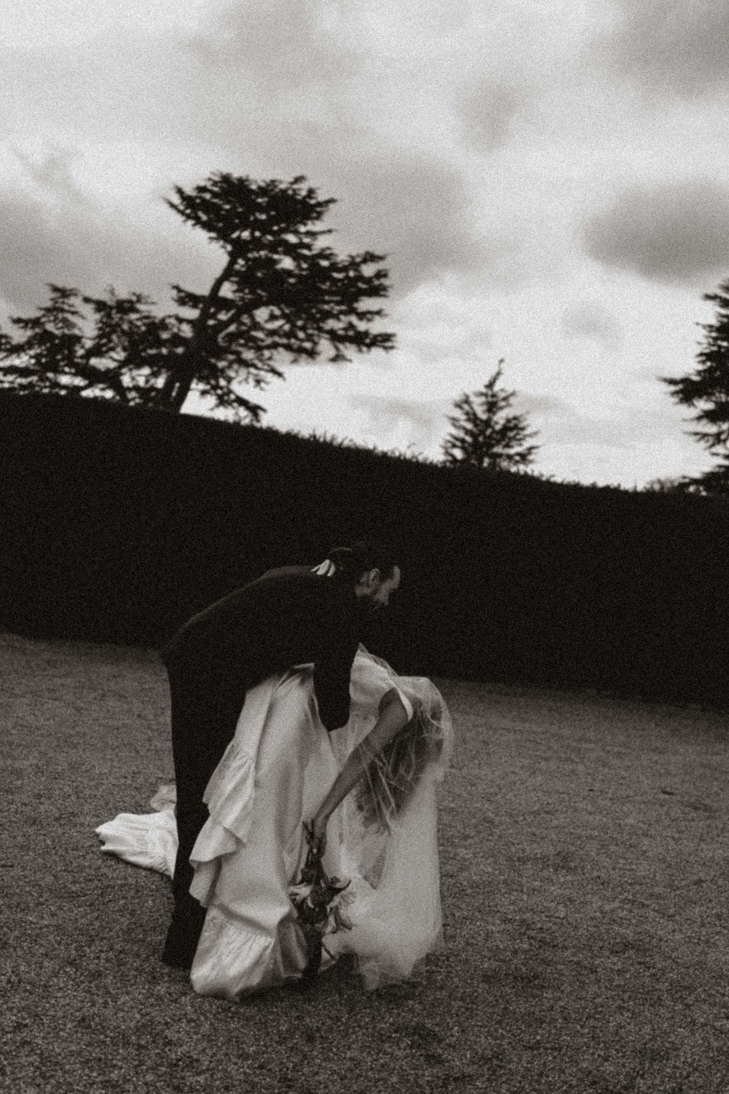 Two figures in flowing white dresses run across a grassy hillside under moody overcast skies.