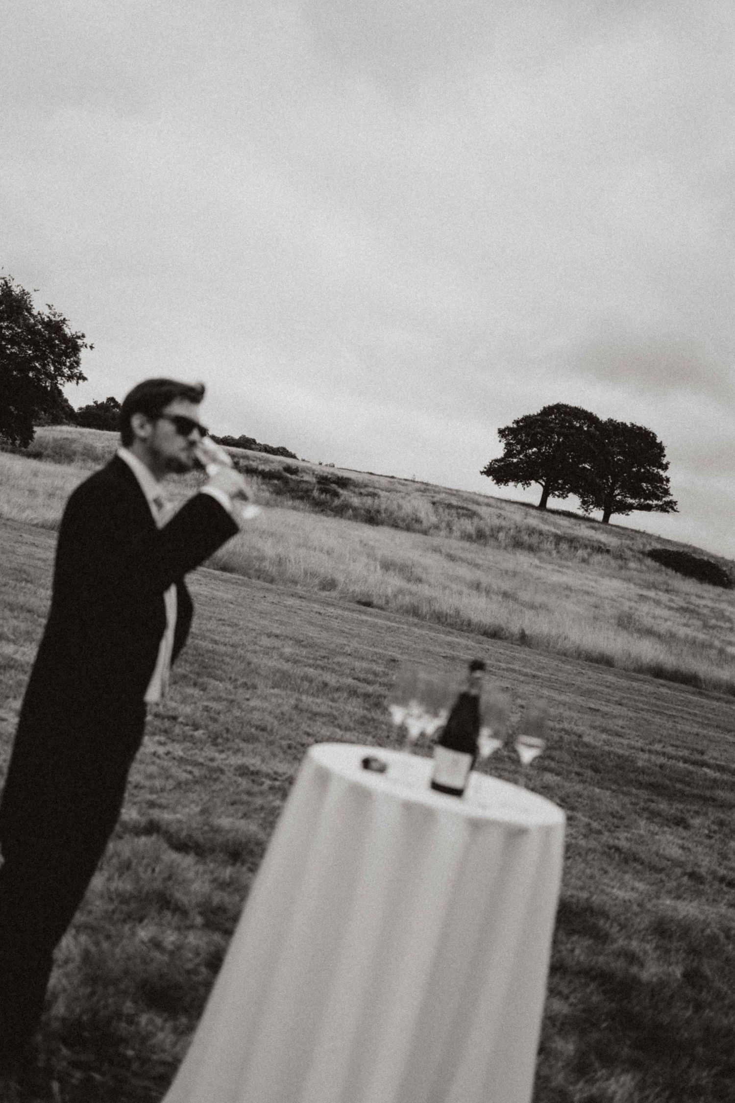 Black and white photo sequence showing someone drinking at a table outside with a solitary tree in the landscape.