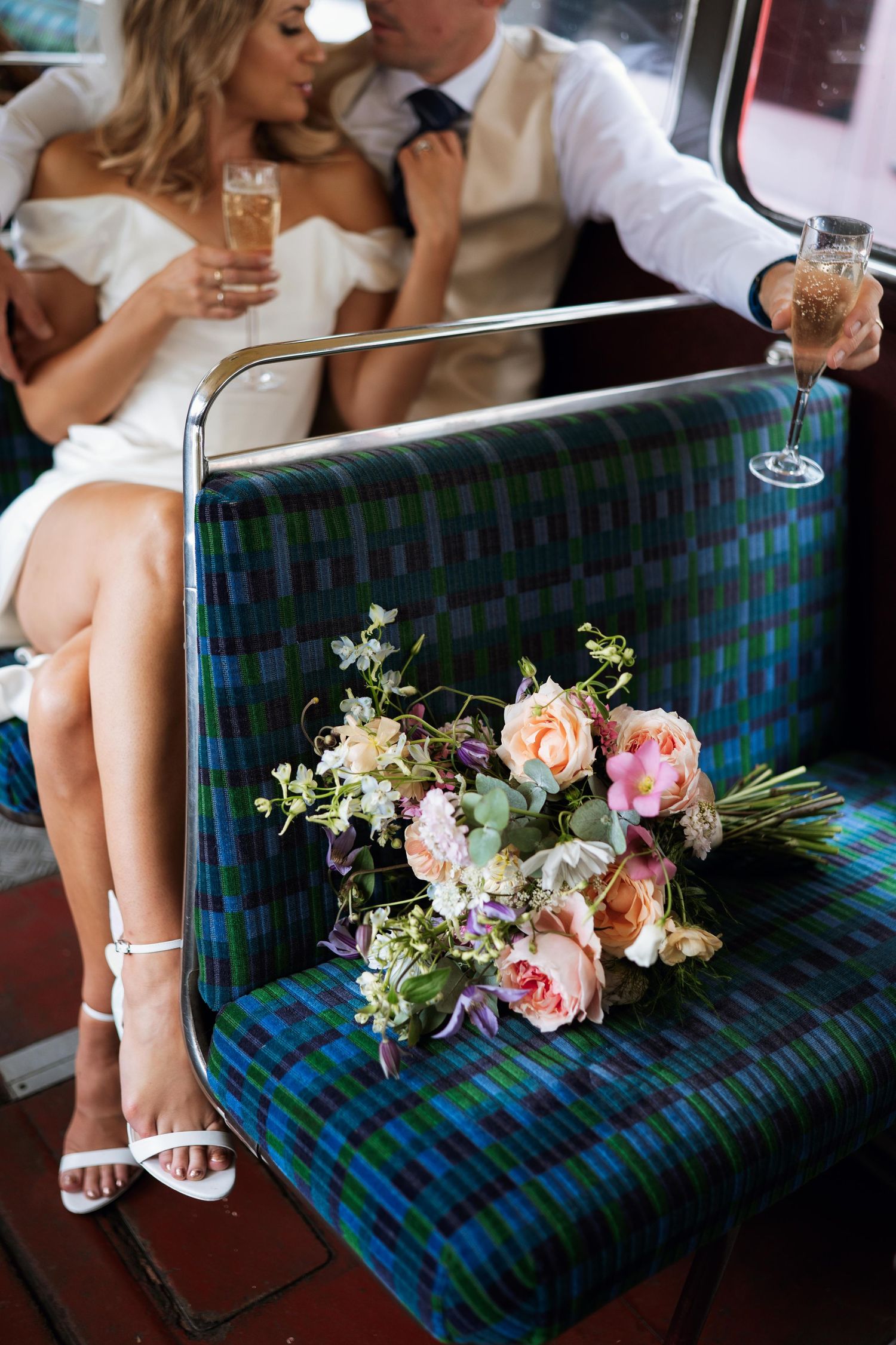 A plaid upholstered bench with a delicate floral bouquet of pink and white flowers resting on its surface.