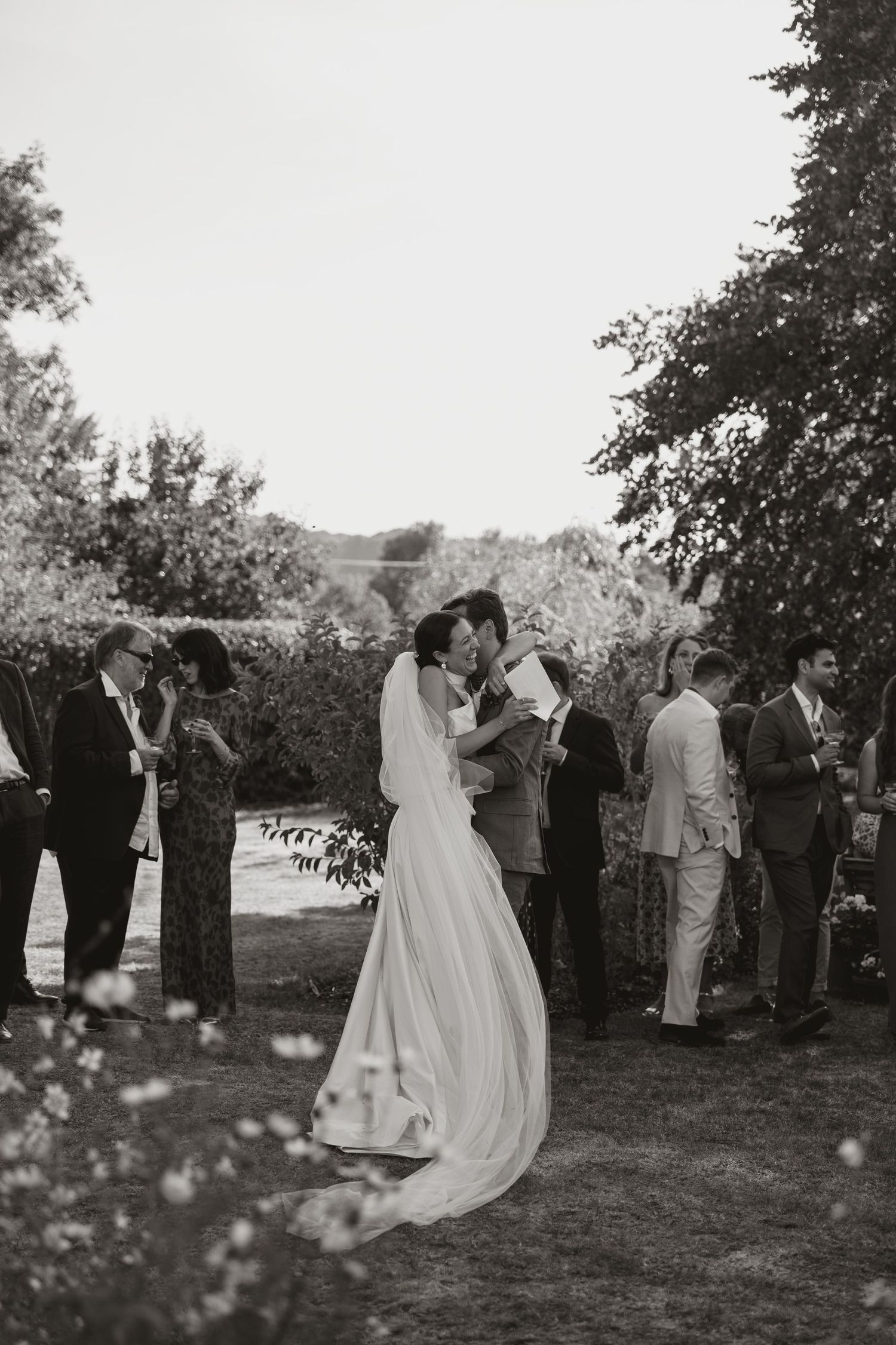 A black and white wedding ceremony photo series showing guests gathered outdoors under trees.
