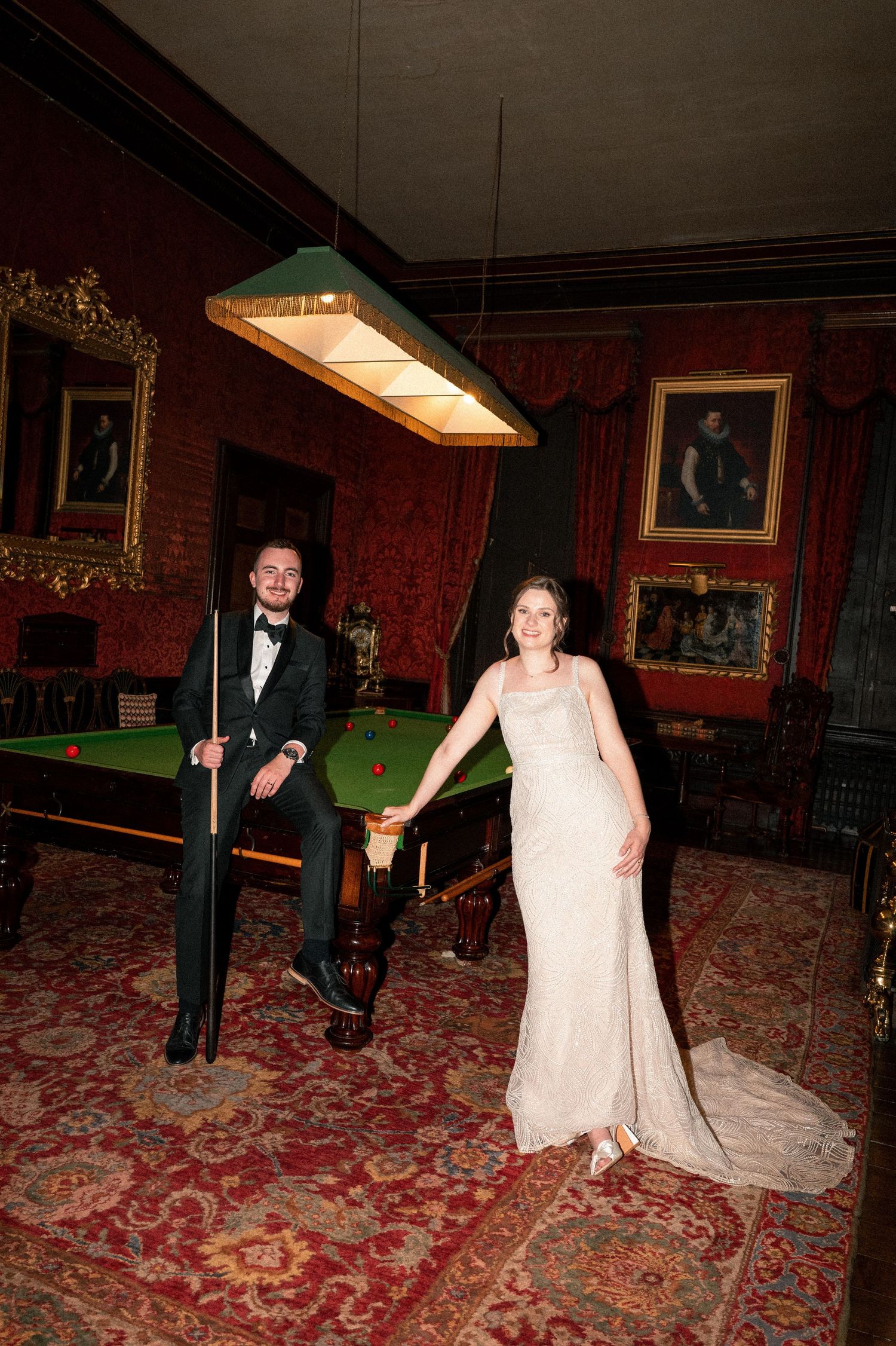 A couple in formal attire dances together in an ornate room with red carpeting and vintage decor.