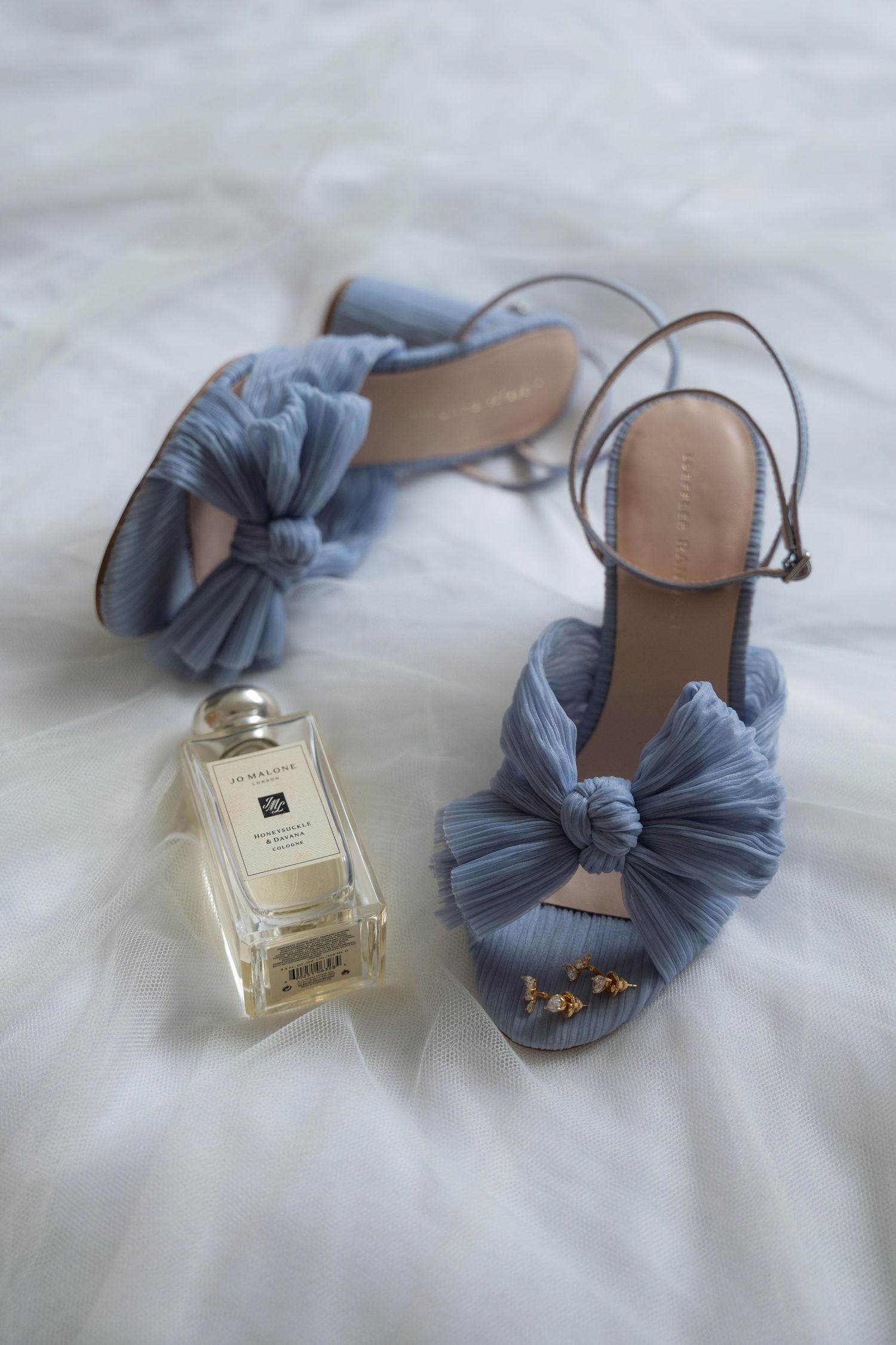 A blue scrunchie hair accessory and perfume bottle arranged on a white textured surface in an aesthetic composition.