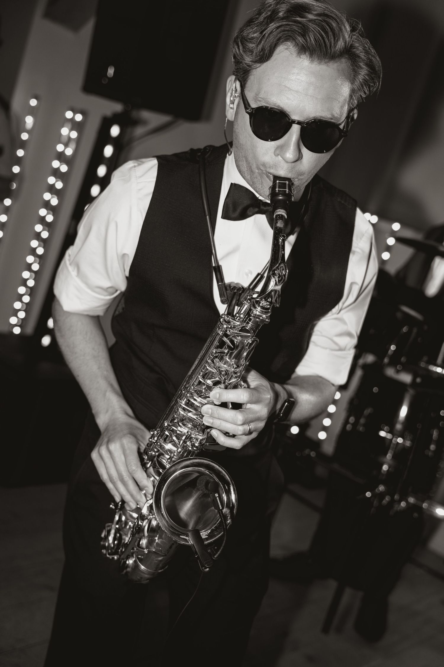 Black and white photos of a saxophone player performing on stage with dramatic lighting and sunglasses.