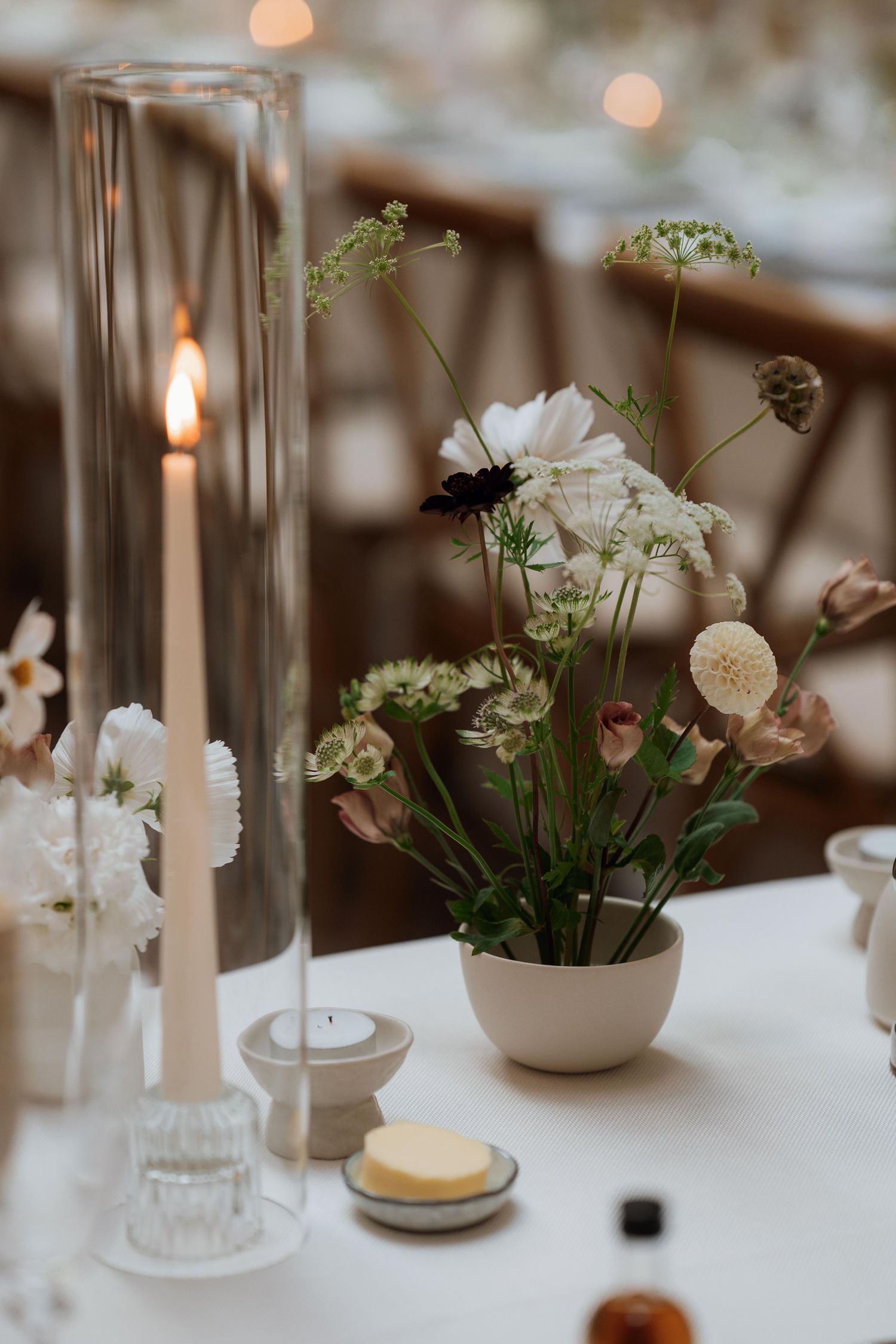 Elegant wedding table setting with white floral centerpieces, taper candles, and soft bokeh lighting in the background.