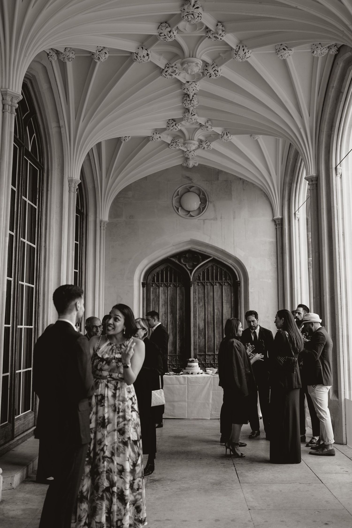 People gather in an elegant Gothic hallway with vaulted ceilings and ornate architectural details at a formal event.