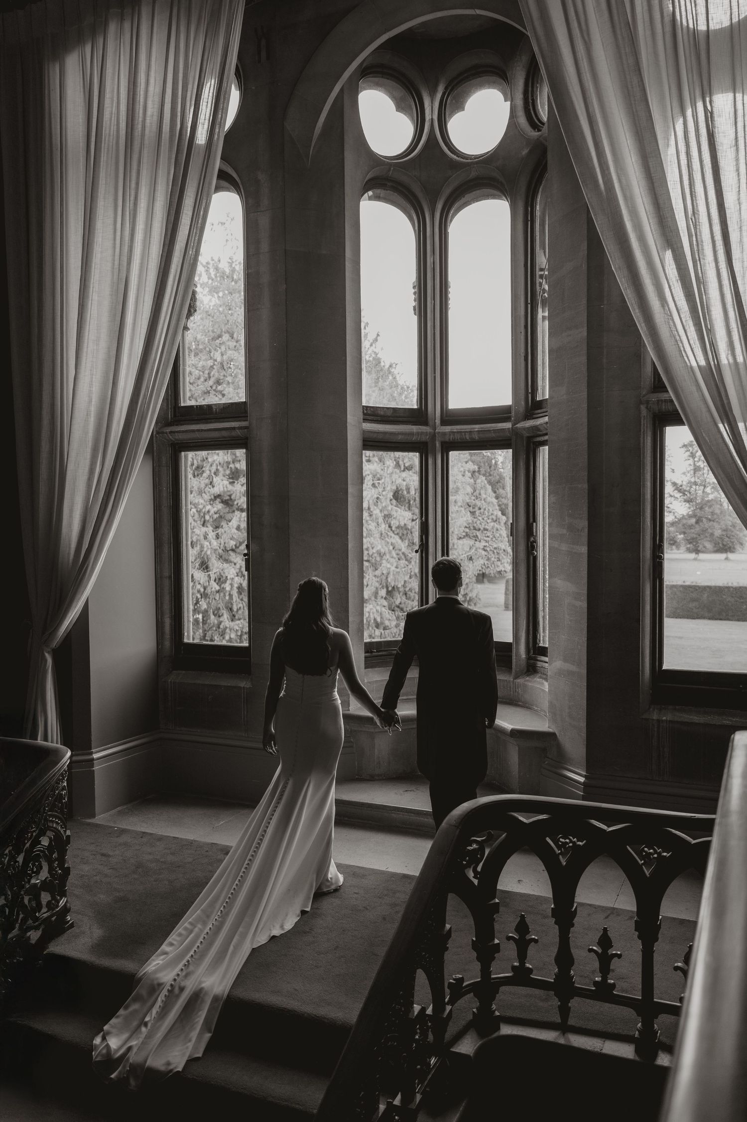 Silhouettes stand near windows with flowing curtains in a moody black and white interior scene.