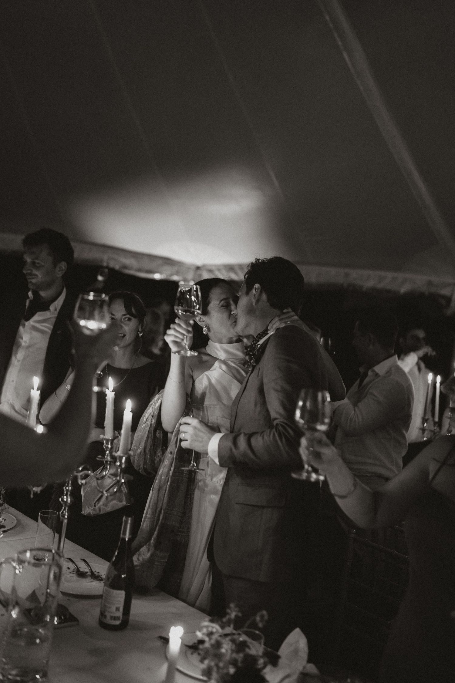 People gathered at a dimly lit bar or party venue socializing and holding drinks in a black and white photograph.