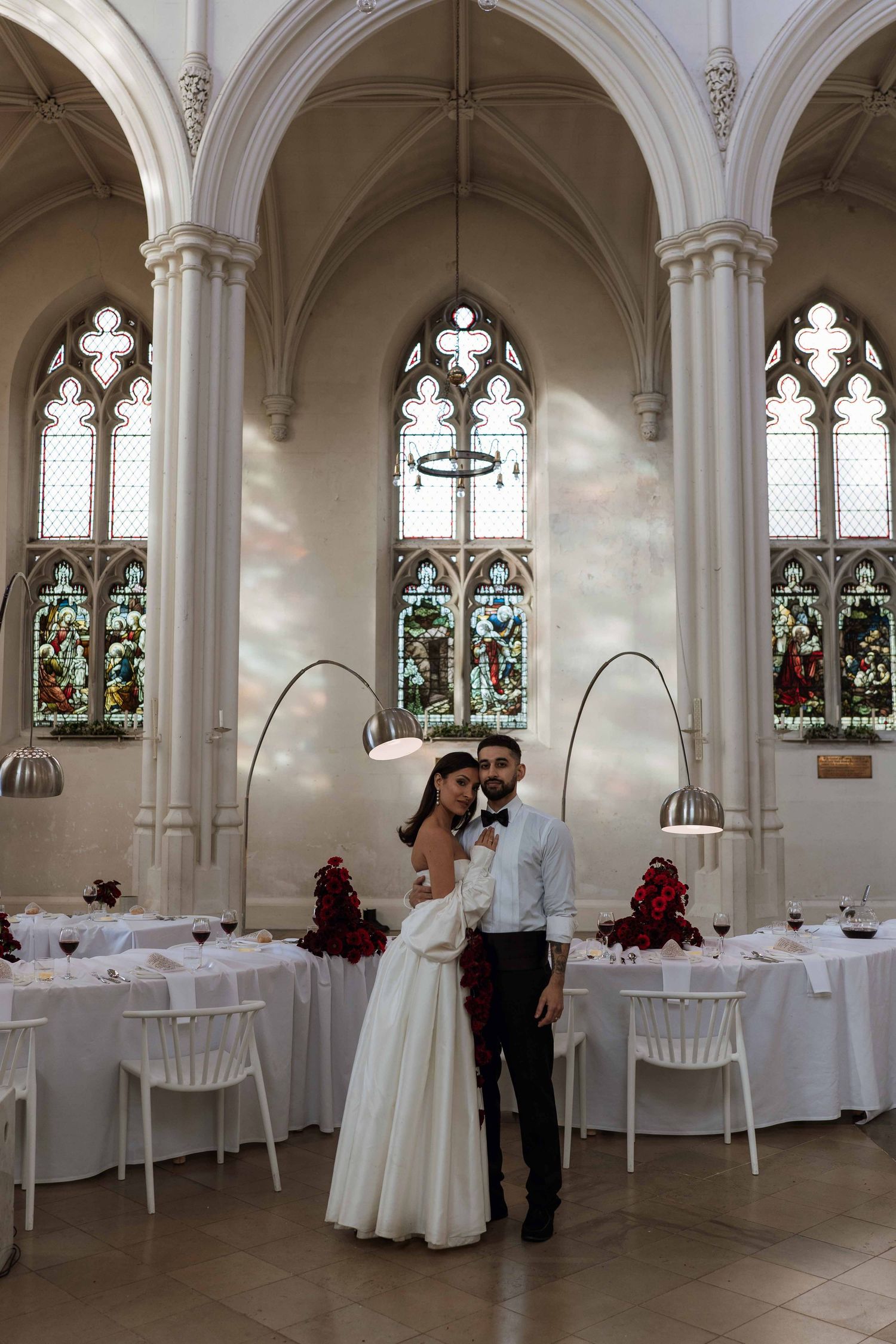 Arched windows and white tables set for an elegant wedding reception in a historic church venue.