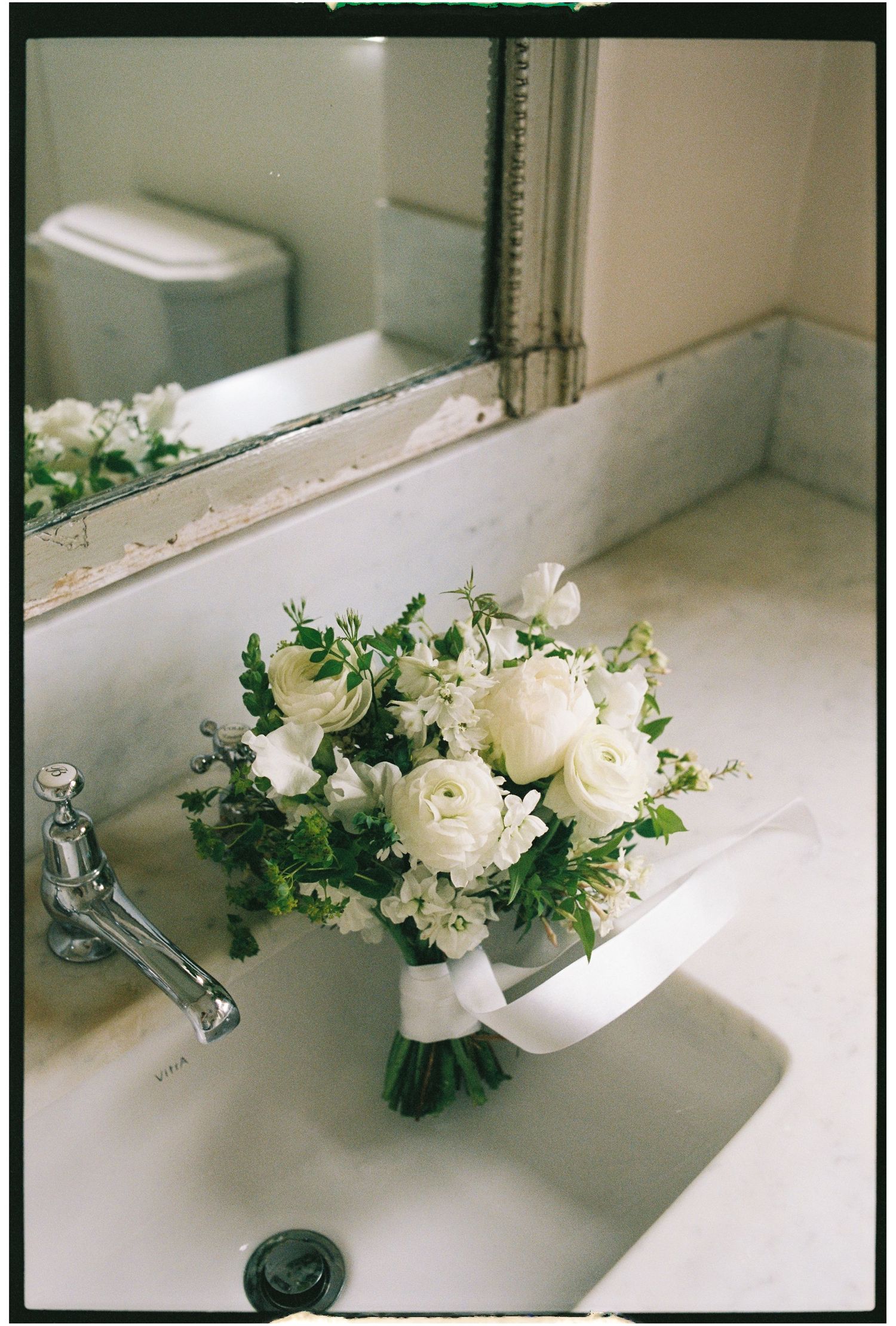 White floral arrangement with delicate blooms and greenery sits elegantly on a bathroom sink counter.