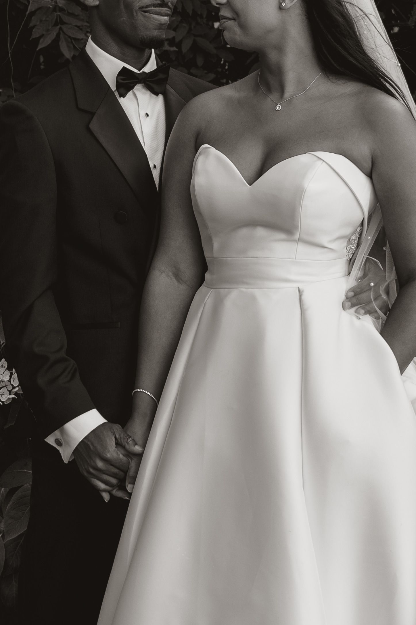 A series of black and white wedding photos showing close-up details of a strapless white wedding dress and formal attire.