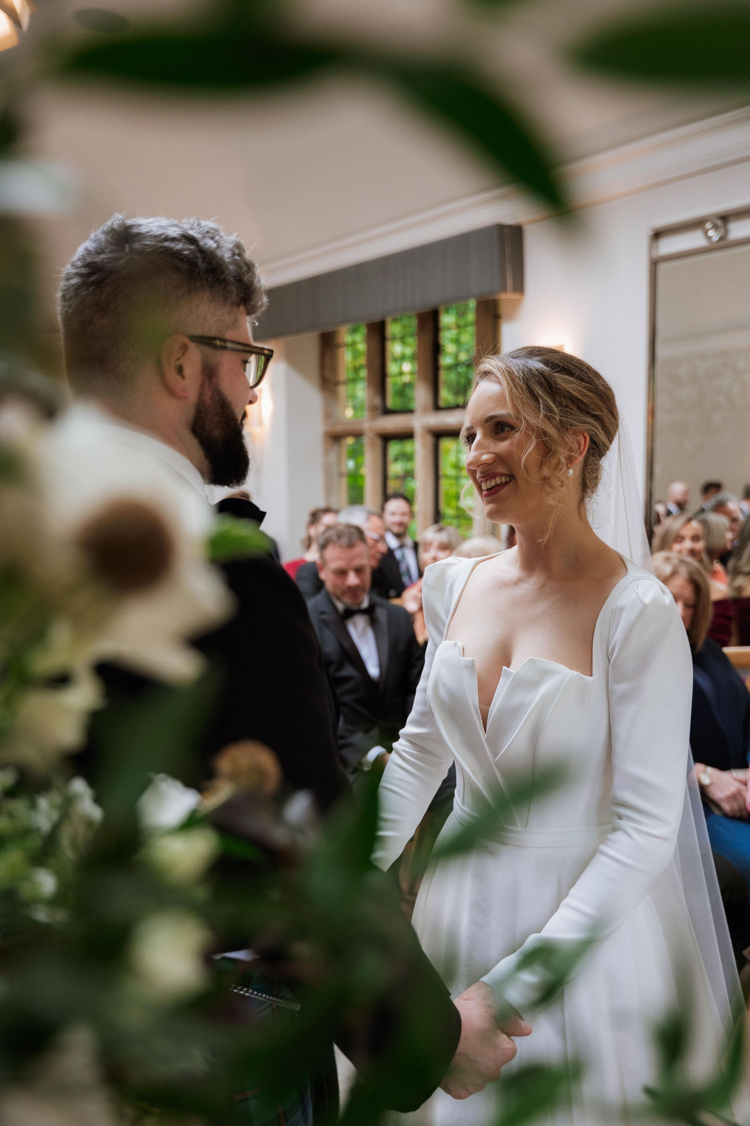 Wedding ceremony guests gather indoors as couple exchanges vows in an intimate venue with natural lighting.