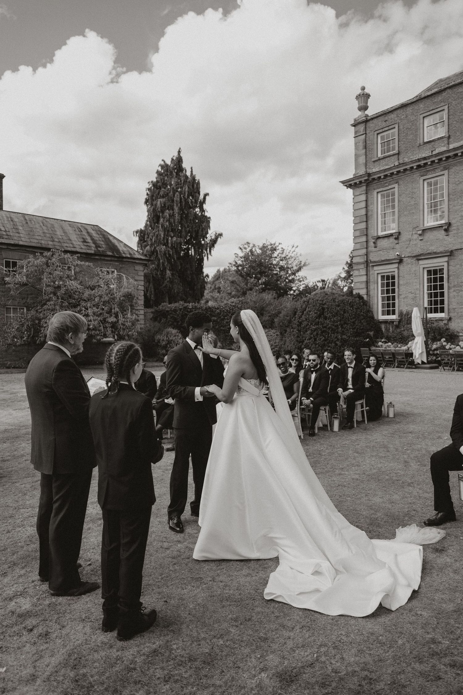 A series of black and white wedding photographs showing a couple and guests on a lawn outside a traditional brick building.