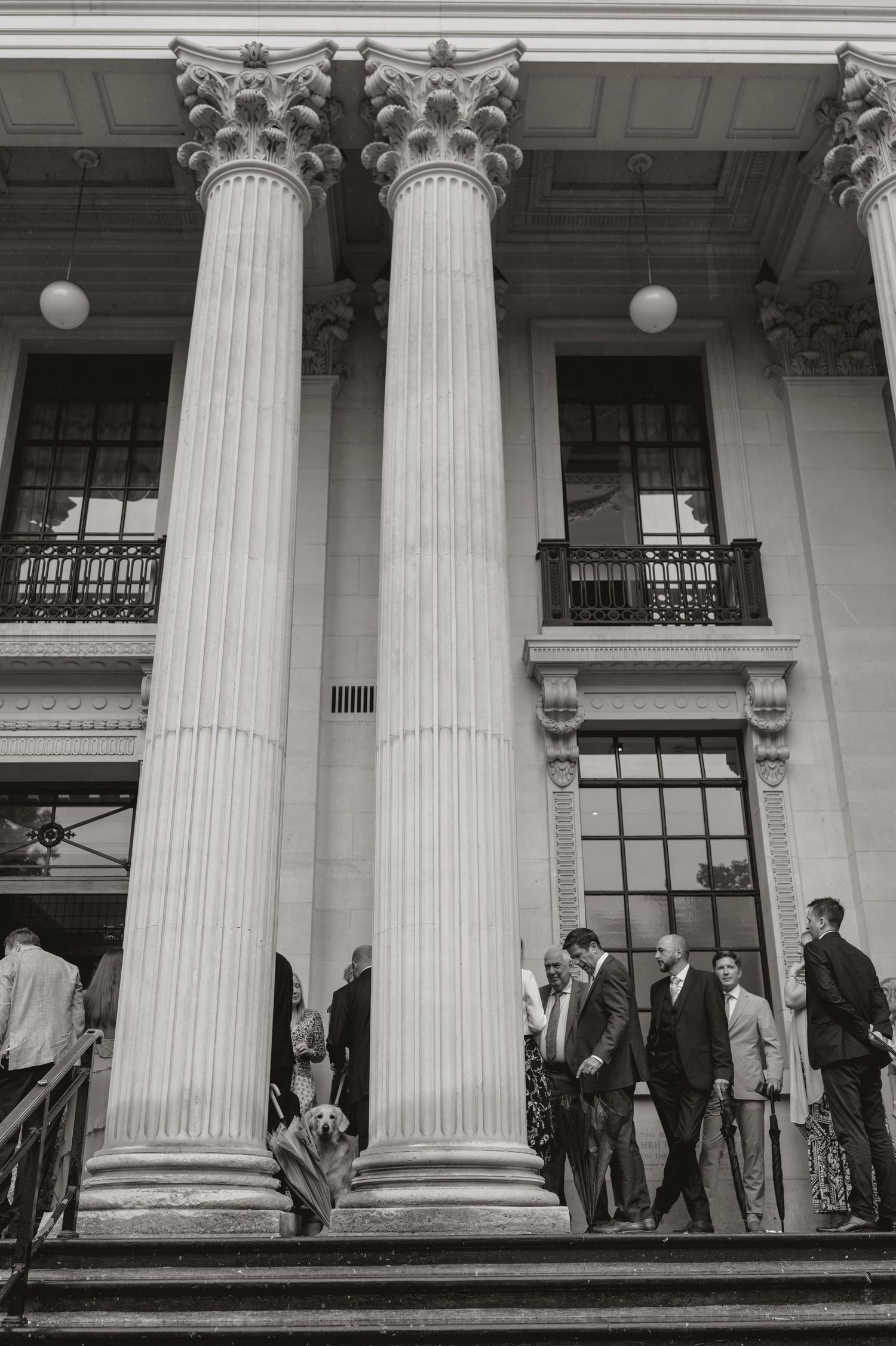 People gathered on the steps of a neoclassical building with white columns and ornate architectural details.