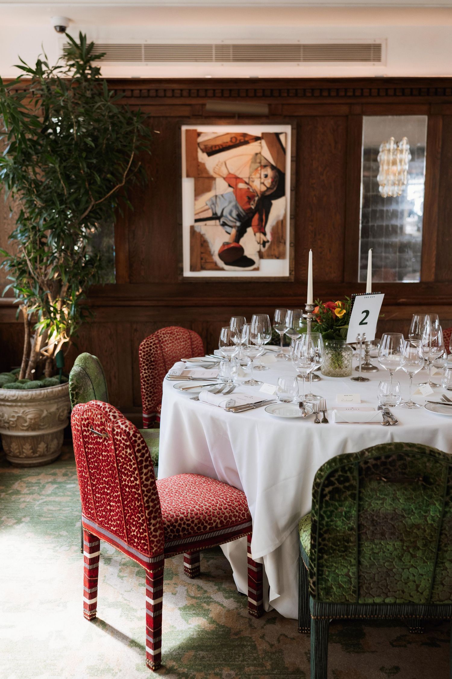 Elegant dining room setup with white tablecloths, red upholstered chairs, and crystal glassware in a traditional restaurant setting.