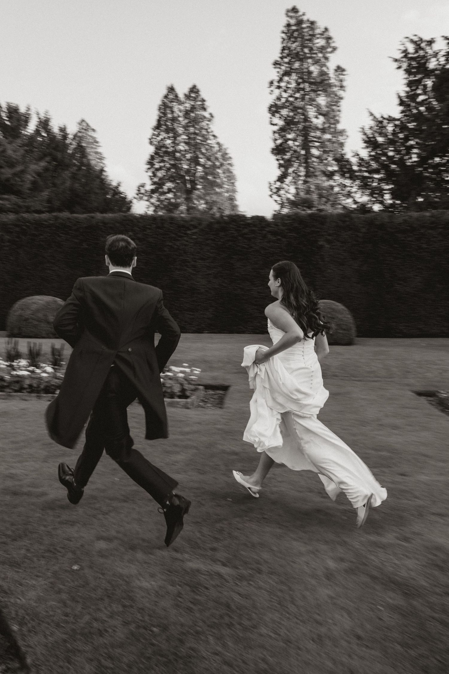 Black and white photo series of a couple in wedding attire playfully running and dancing together in a grassy field.