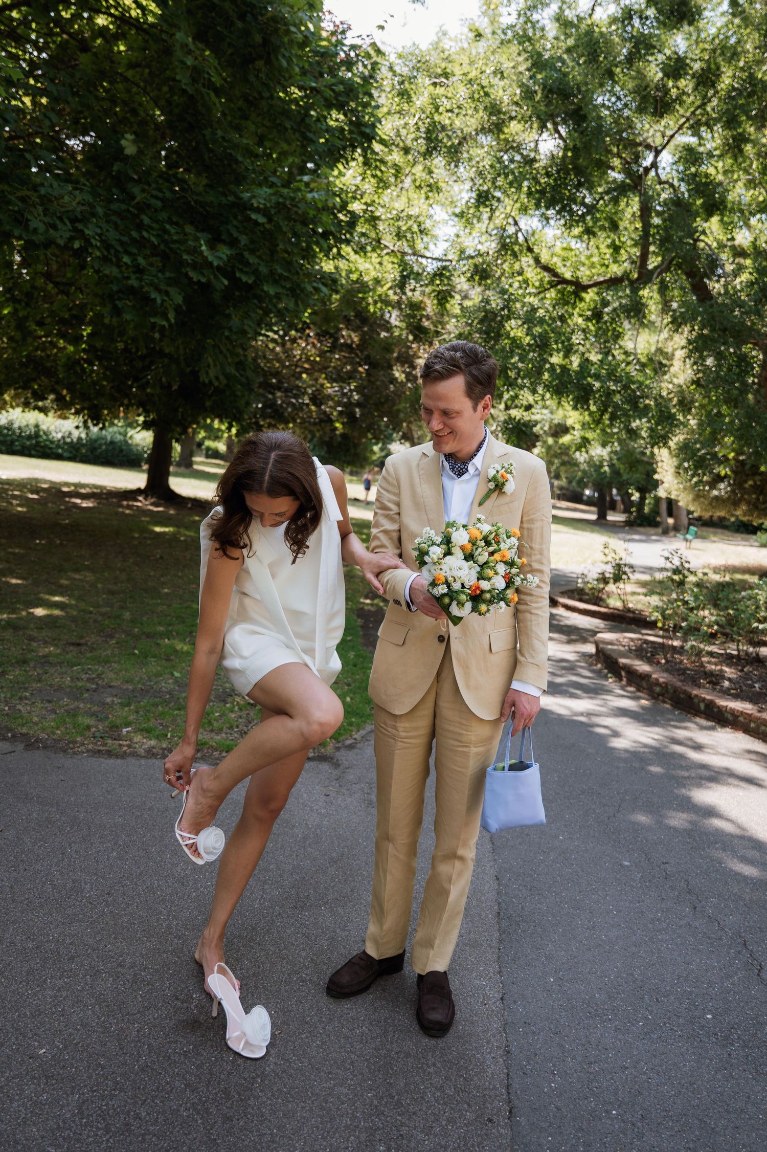 A sequence of wedding photos showing a couple playfully adjusting their shoes on a paved path in a park setting.