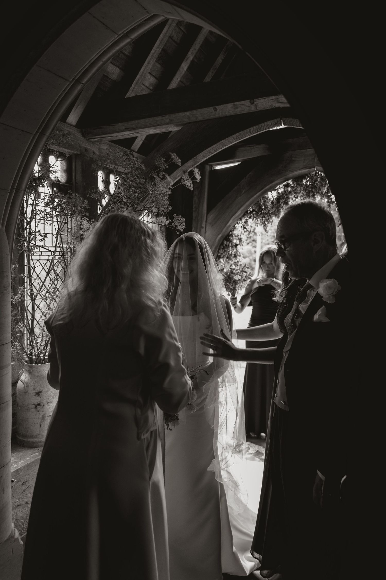 A black and white wedding ceremony photo showing figures standing under a gothic church archway with stained glass windows.