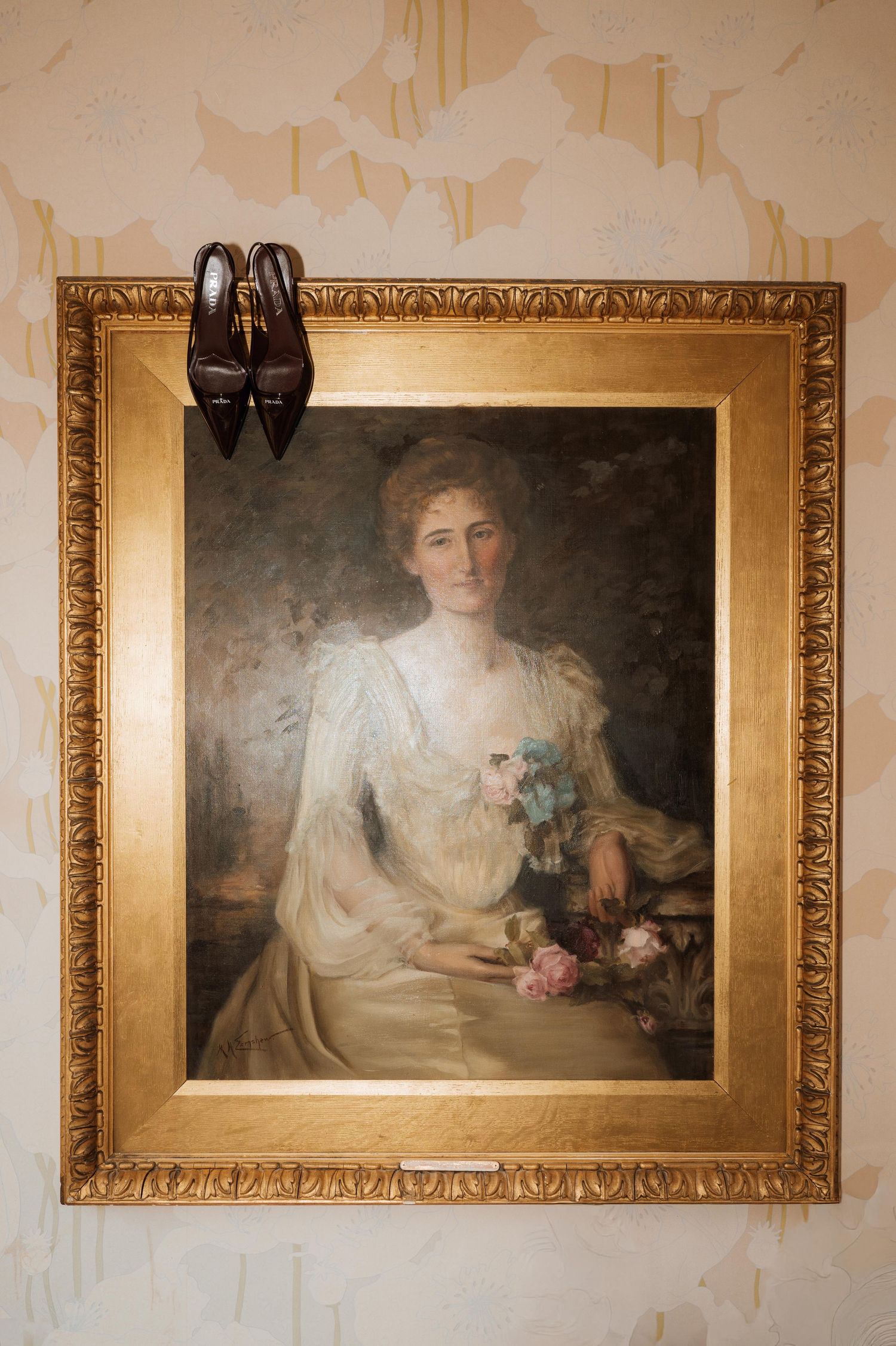 Three vintage portrait paintings in ornate gold frames hang on a cream-colored wall in a gallery setting.