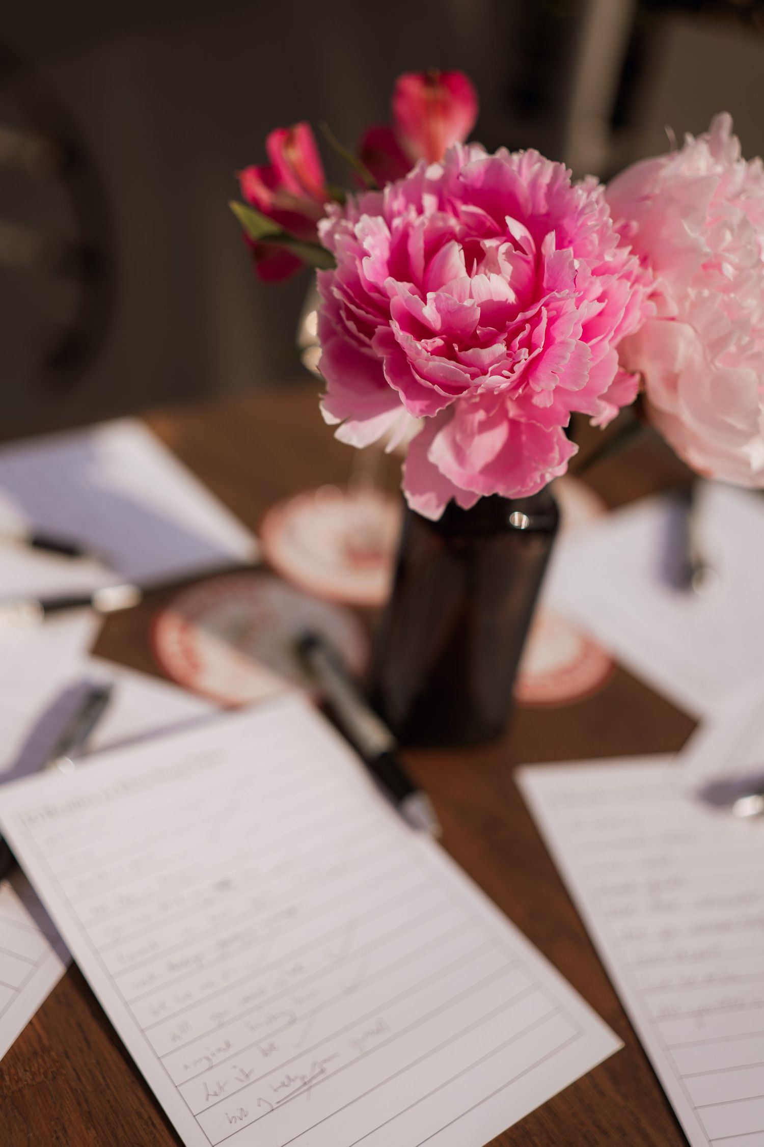 Pink carnation flowers rest atop handwritten notes on a dark wooden table surface.