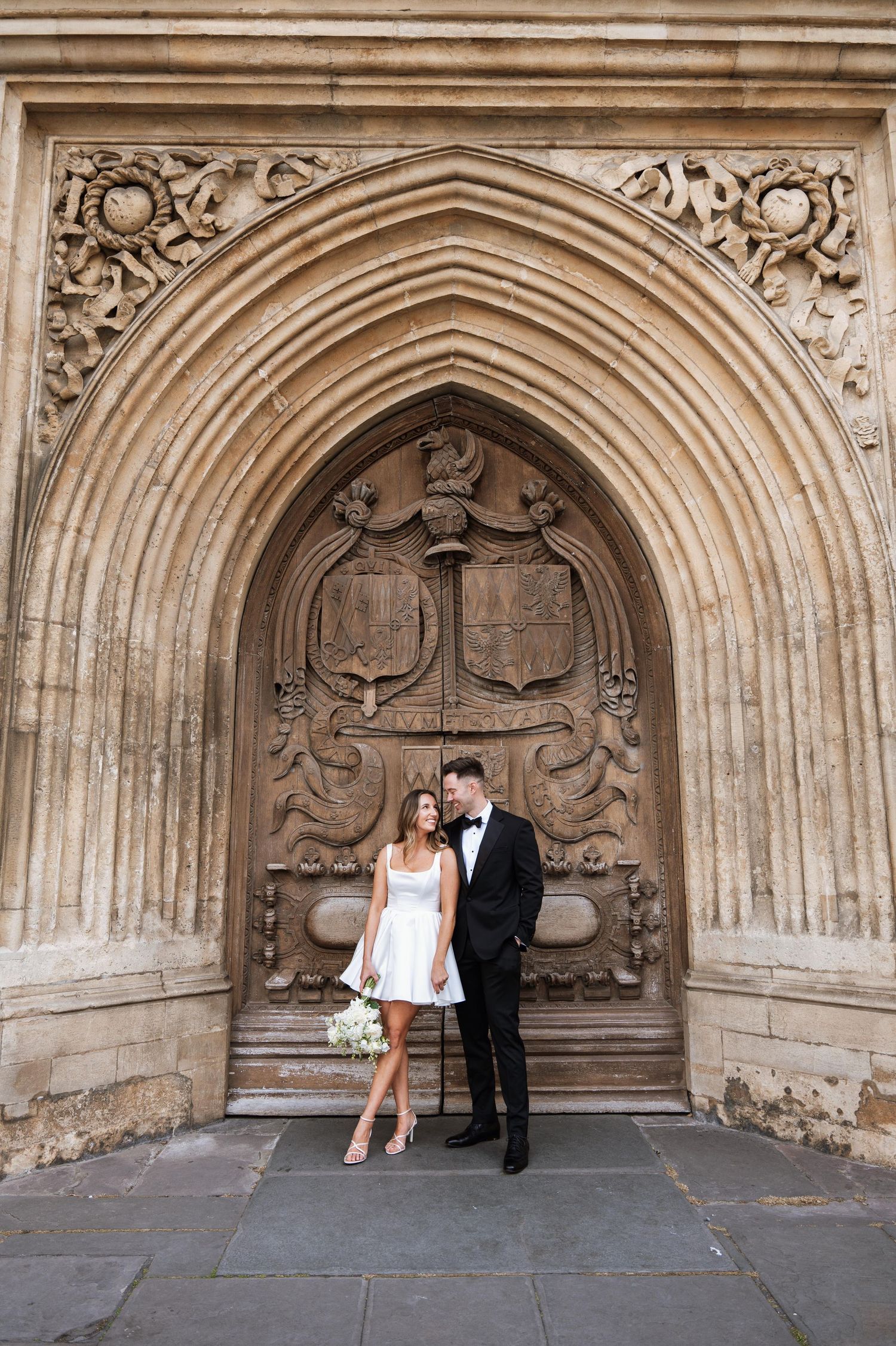 Wedding couple poses in sequence under ornate stone archway with decorative gothic architectural details.