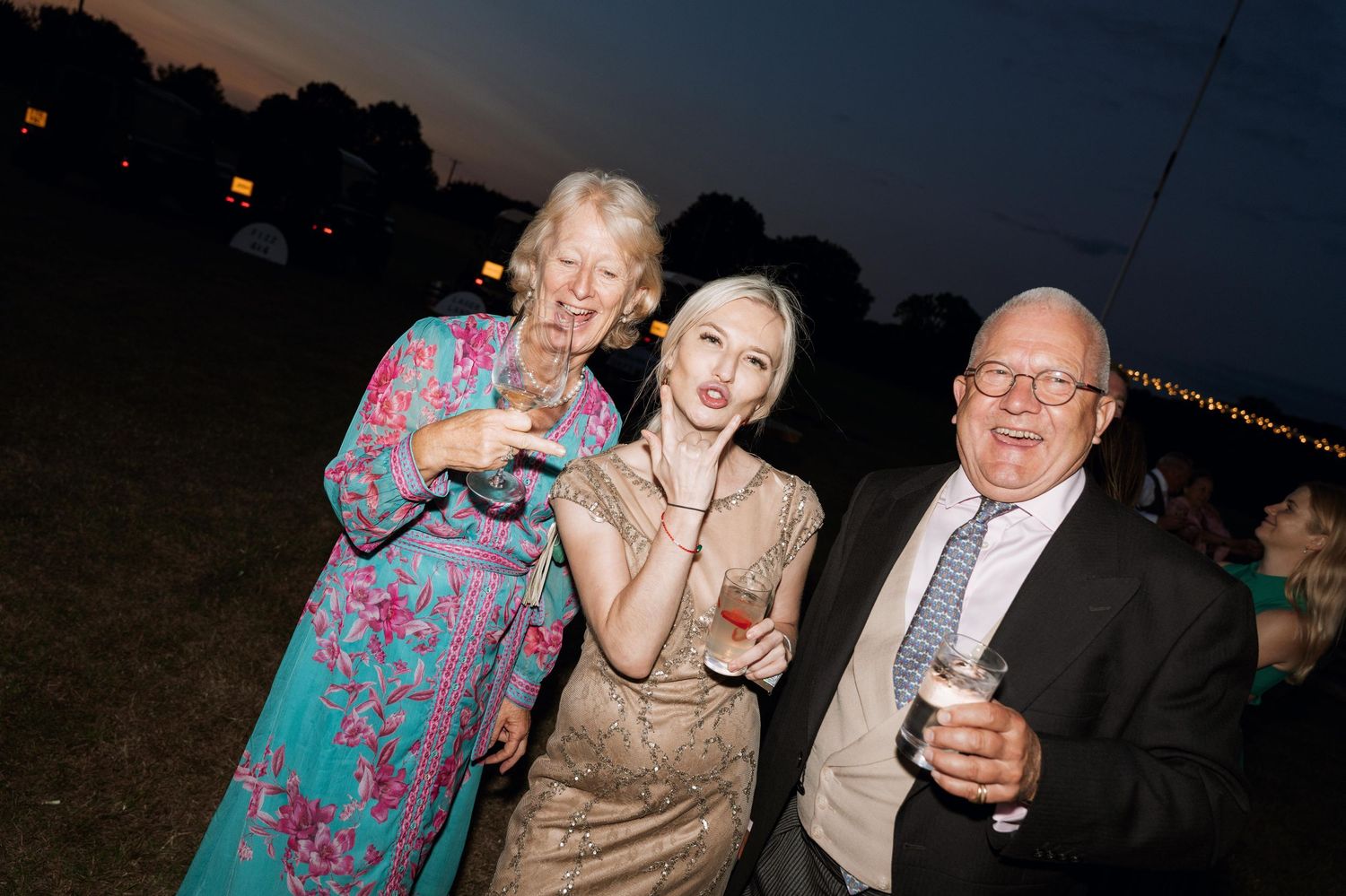 People enjoying a nighttime outdoor event with drinks and laughter against a dark sky backdrop.