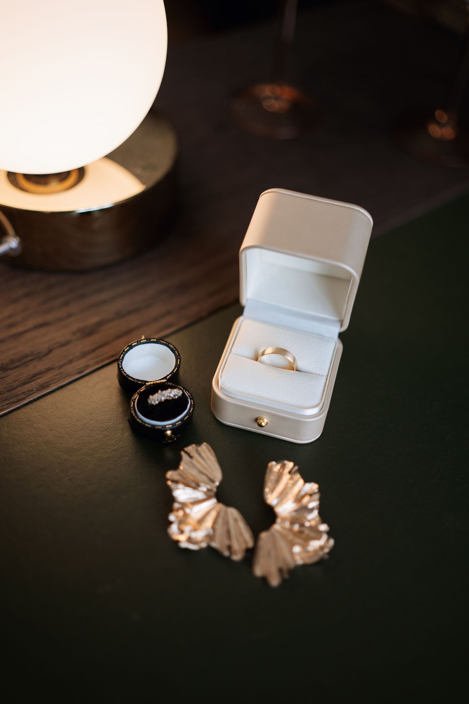 Wedding rings and jewelry displayed in white boxes on a dark wooden surface with dramatic lighting.