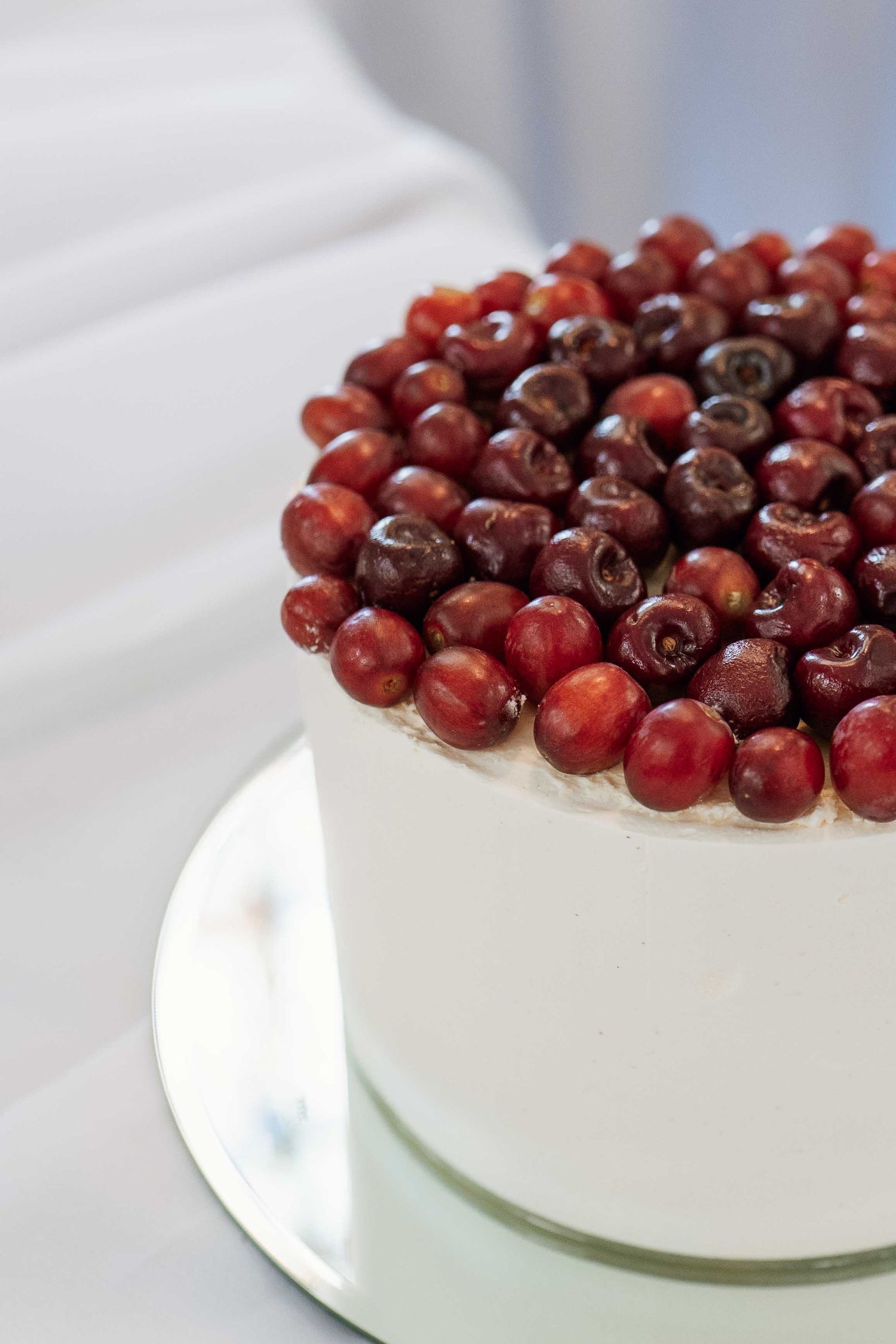 White frosted cake topped with fresh red cranberries arranged in a circular pattern on a white plate.